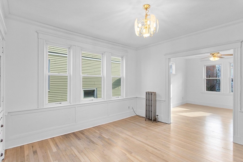 Empty living room with hardwood floors, three tall windows, and a chandelier.