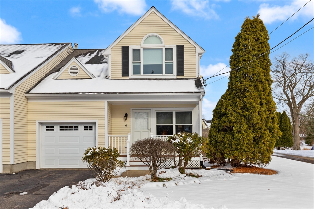 Beige two-story house with an attached garage and covered porch, surrounded by snow and a tall evergreen.