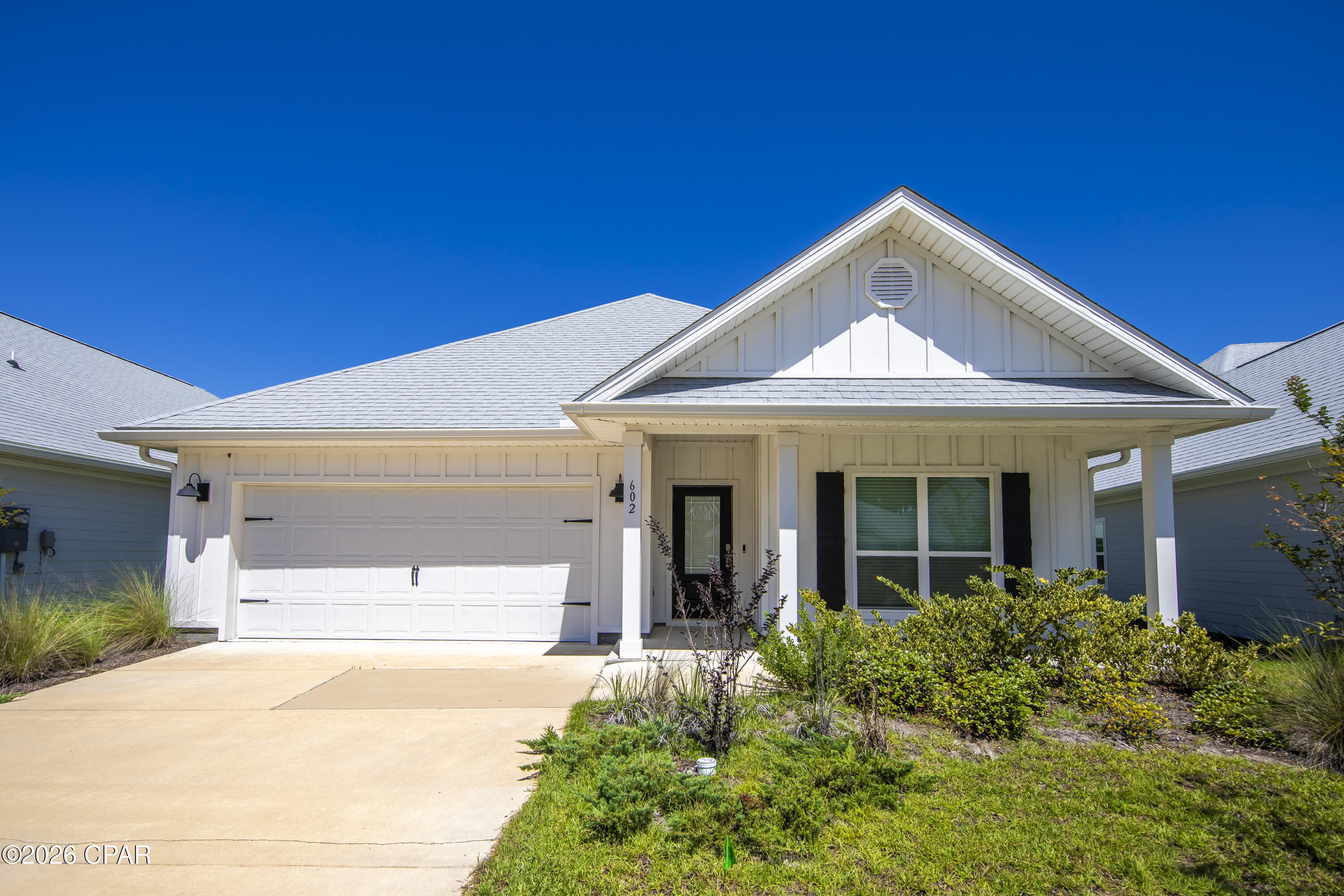 White single-story home with a steep front gable, two-car garage, covered porch, and landscaped yard.