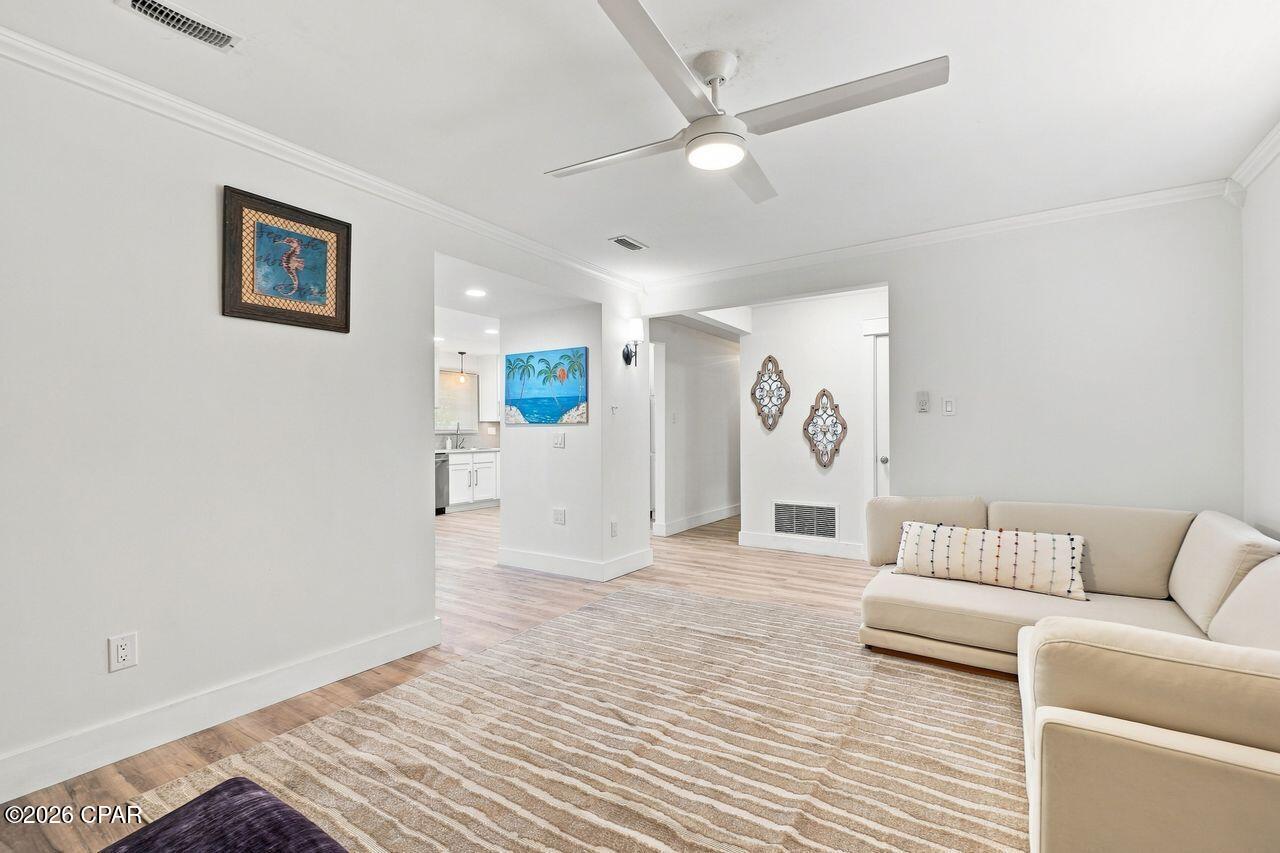 Living room with a cream sectional, striped rug, ceiling fan, and open view toward the kitchen.