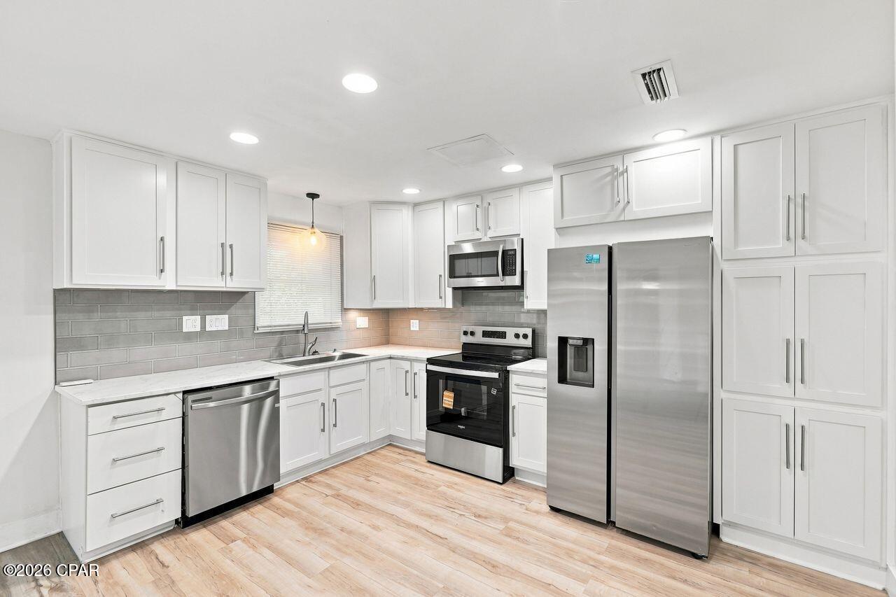 Renovated kitchen with white cabinets, gray tile backsplash, and stainless steel appliances.