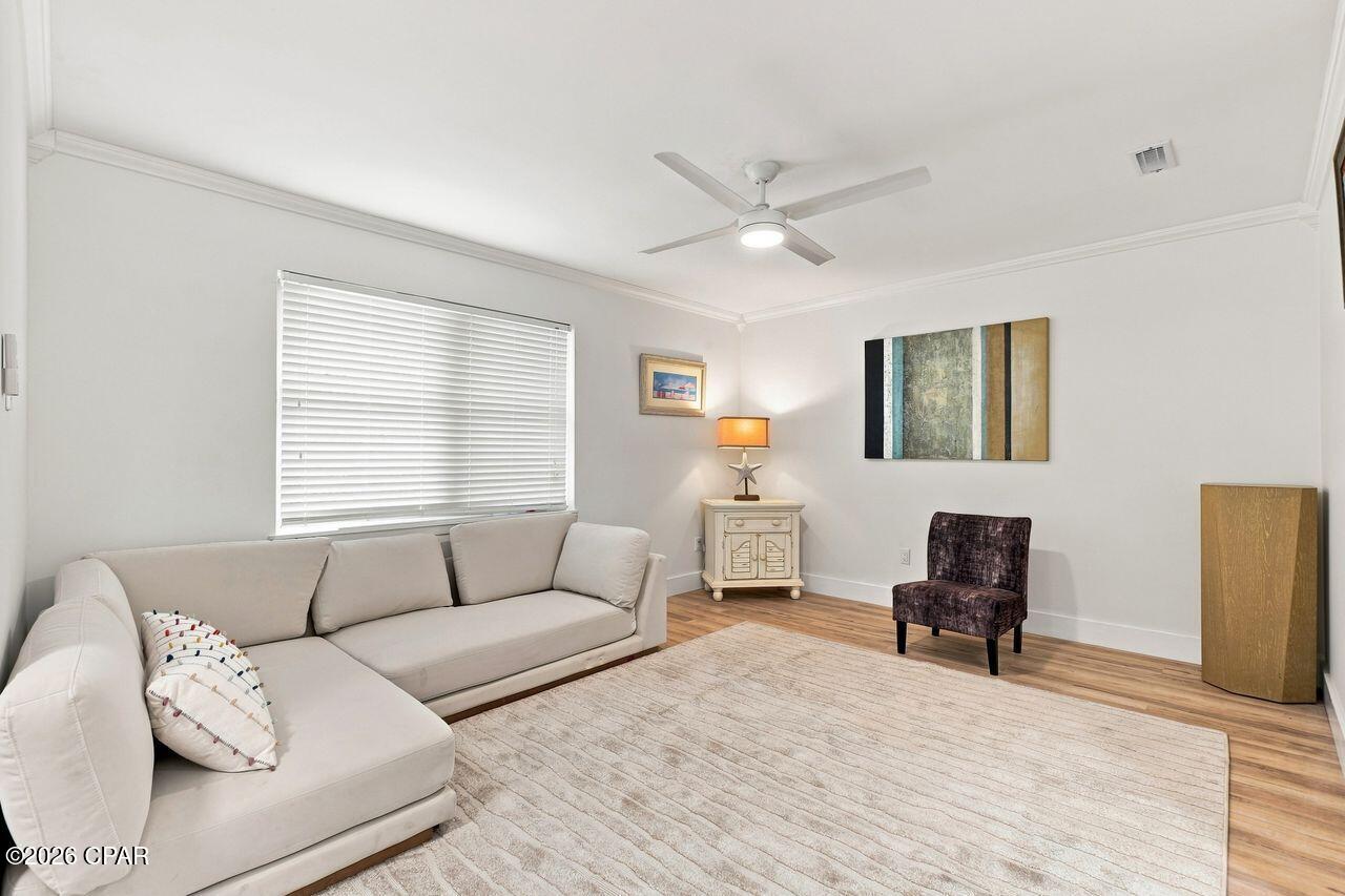 Living room with a white sectional, pale rug, wood floors, and ceiling fan.