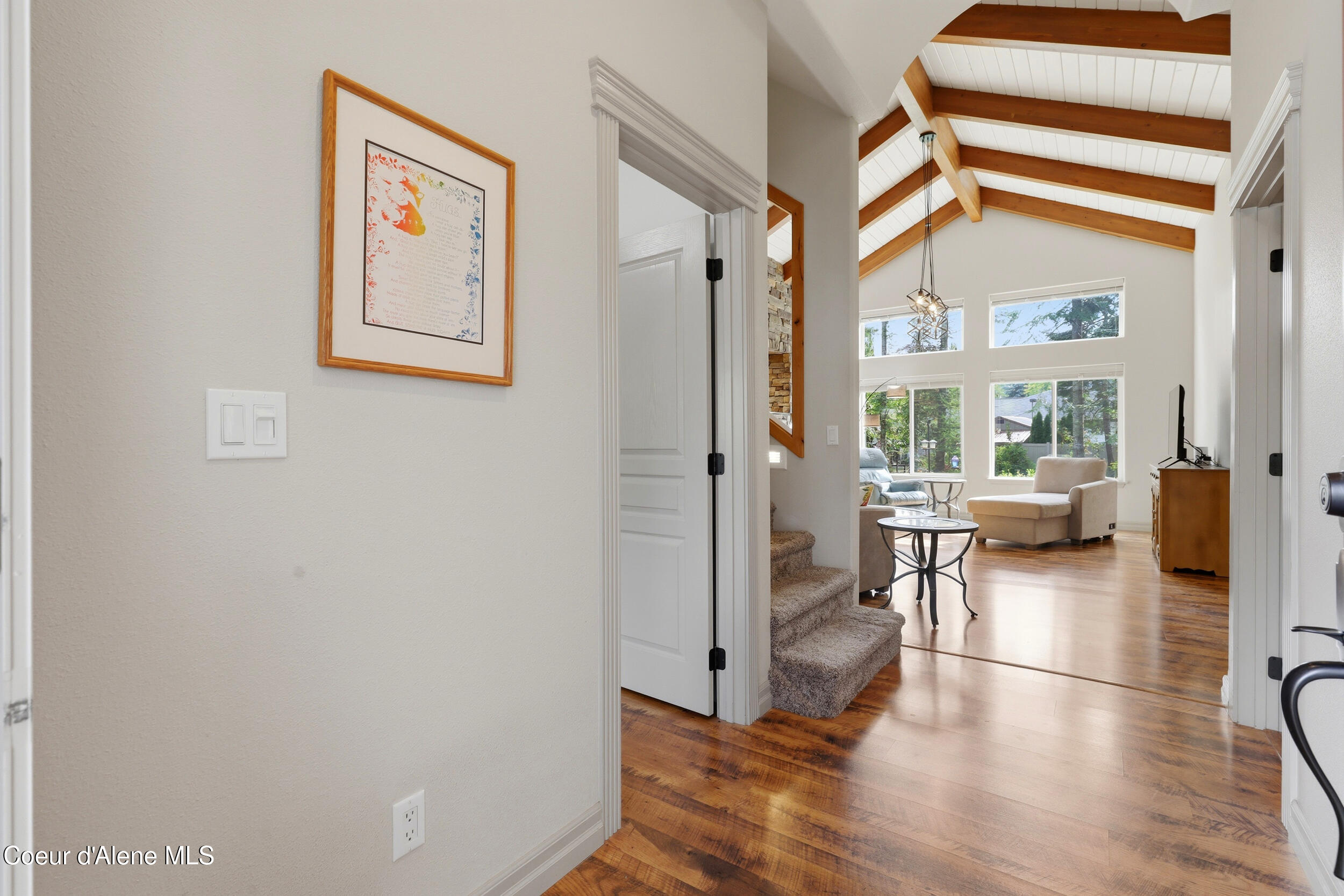 Living room with vaulted wood-beam ceiling, tall windows, hardwood floors, and an adjacent staircase.