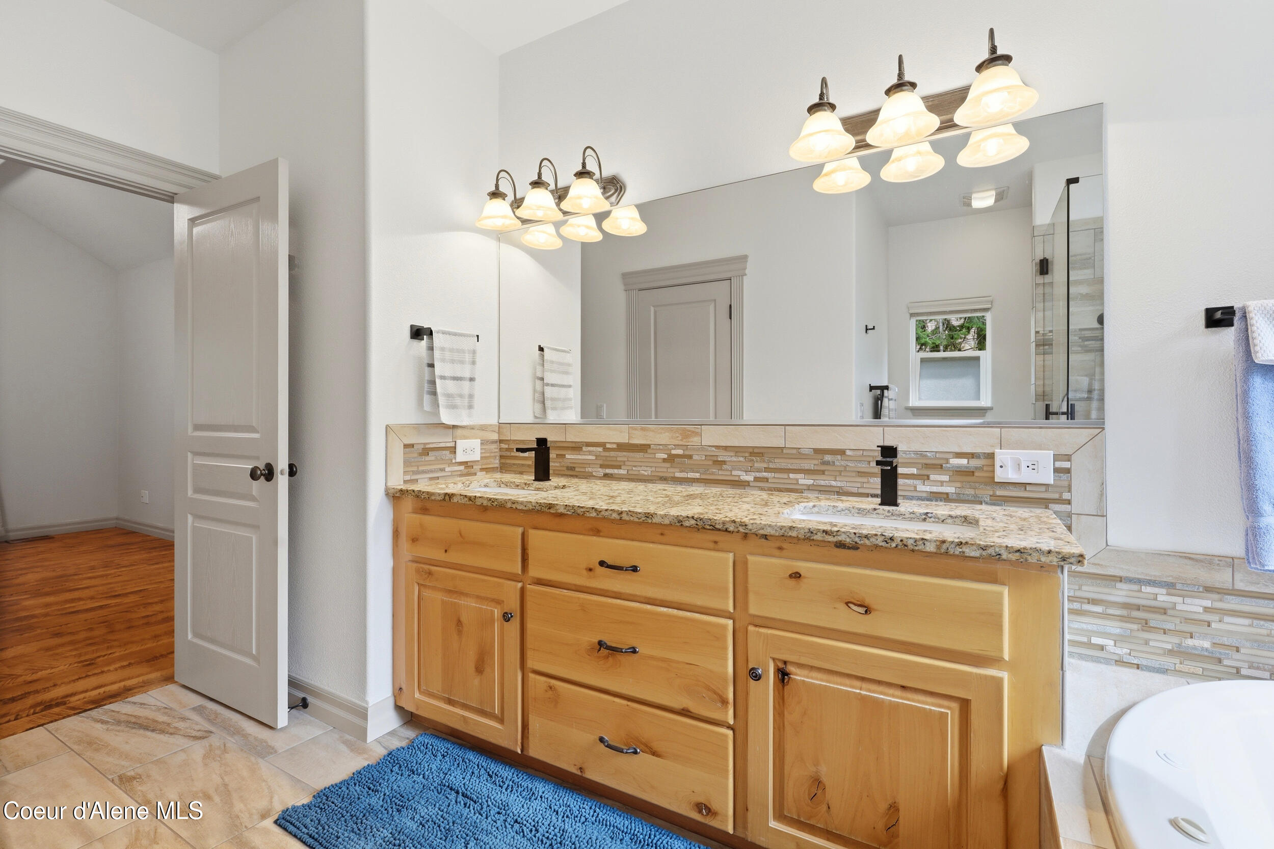 Bathroom with a double-sink wood vanity, granite countertop, and mosaic tile backsplash.