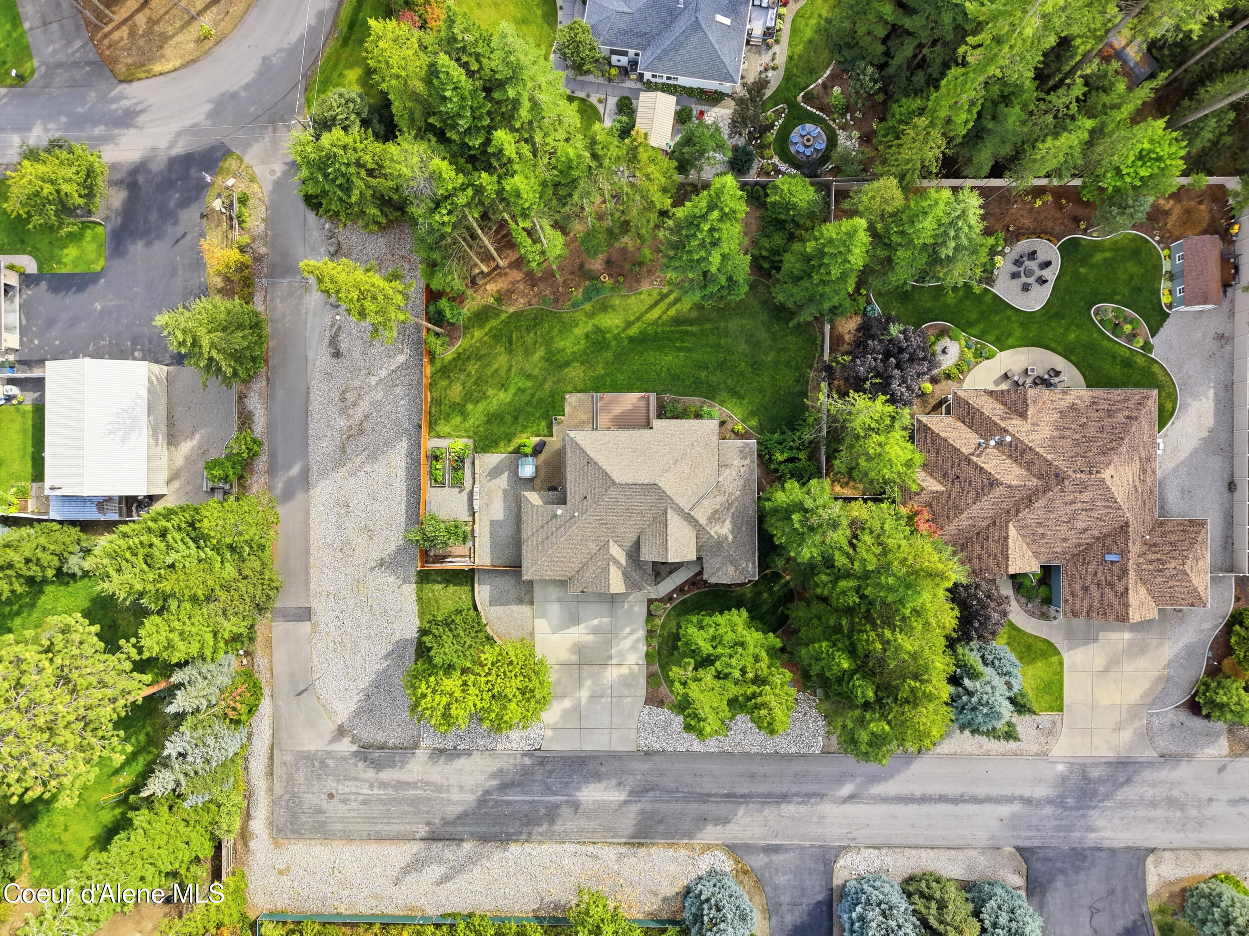 Aerial view of the home, showing a broad landscaped lawn, mature trees, and paved outdoor seating areas.