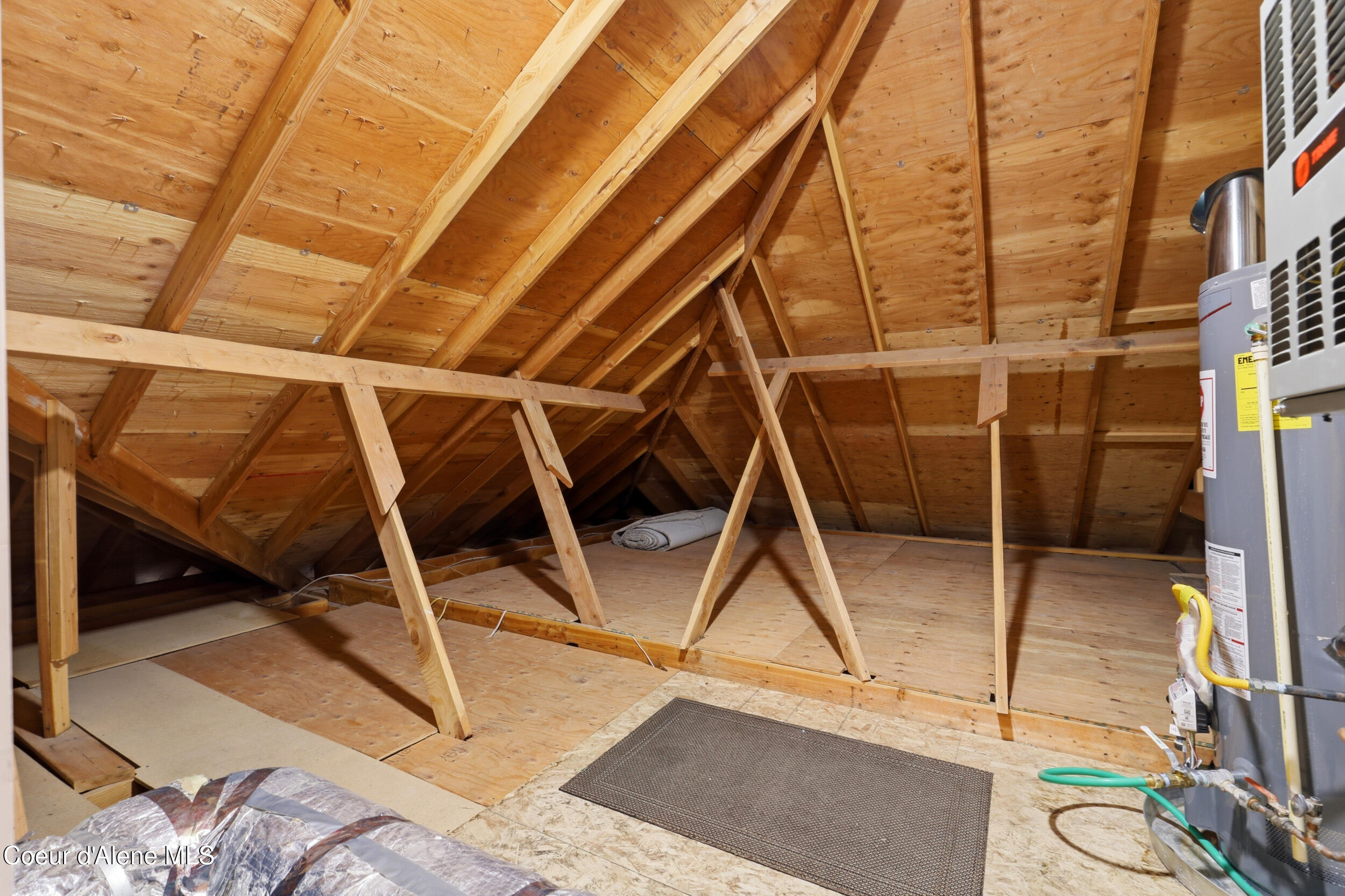 Unfinished attic with exposed wooden rafters, plywood flooring, and a water heater.
