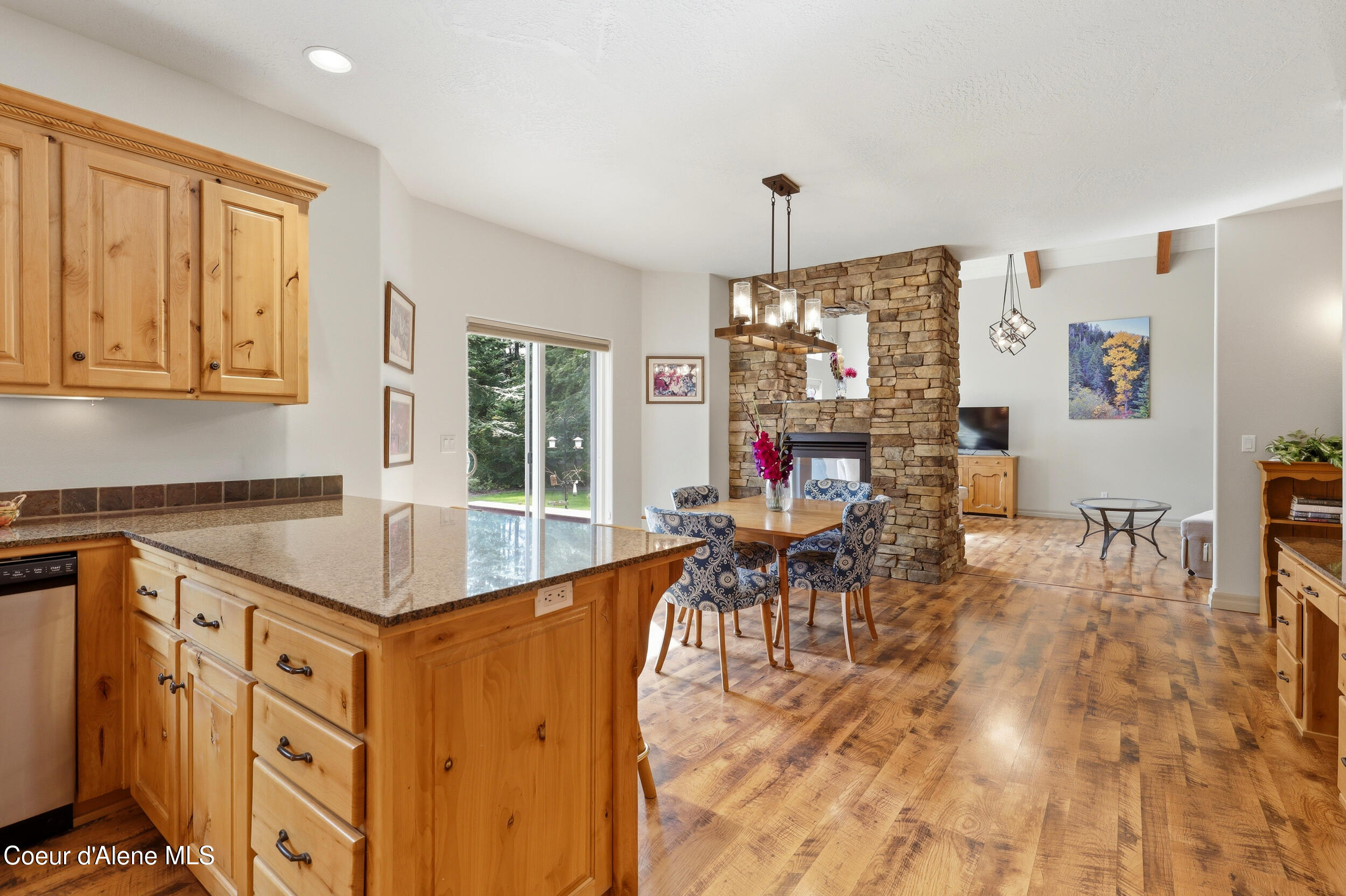 Open-plan kitchen and dining area with a granite island, wood cabinetry, and a large stone fireplace.