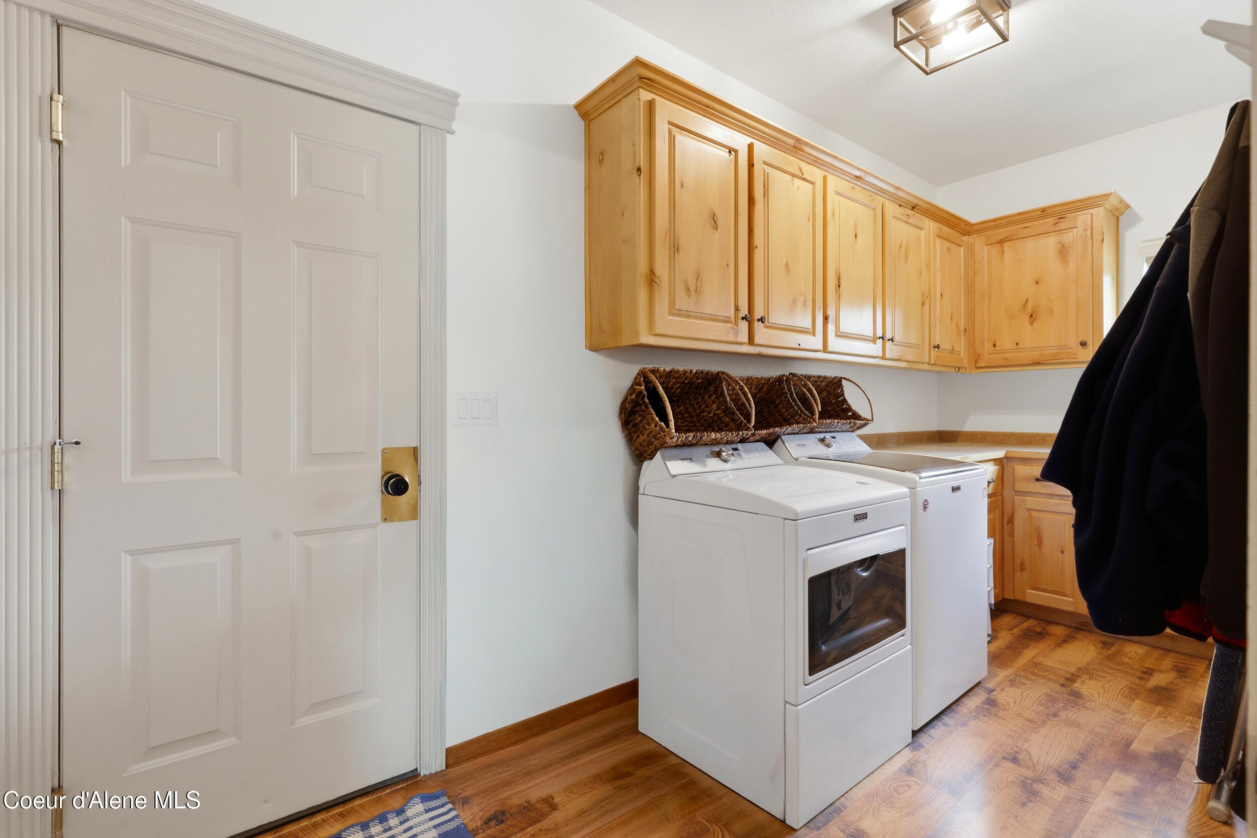 Laundry room with white washer and dryer, honey-toned cabinets, and wood-look flooring.