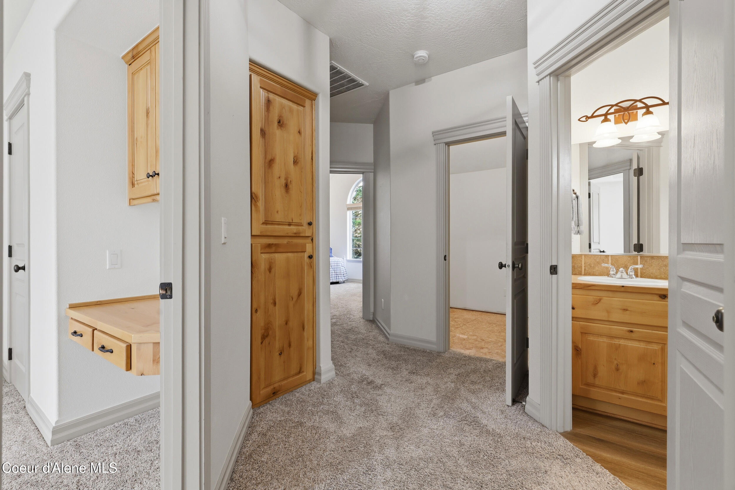 Carpeted hallway with built-in wood cabinets, opening to a bathroom and bedroom.