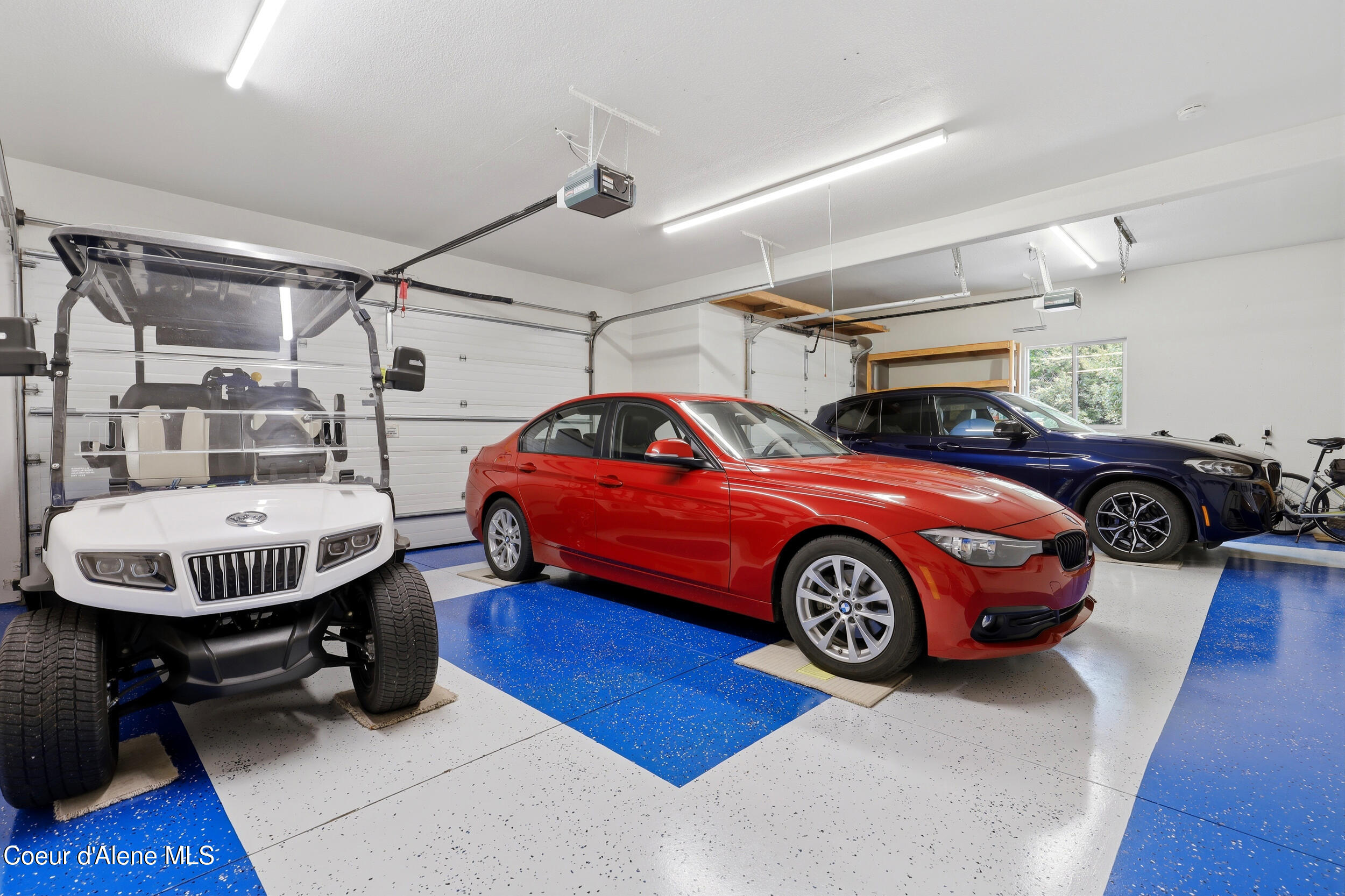 Spacious garage with a blue-and-white floor, two cars, and a white golf cart.