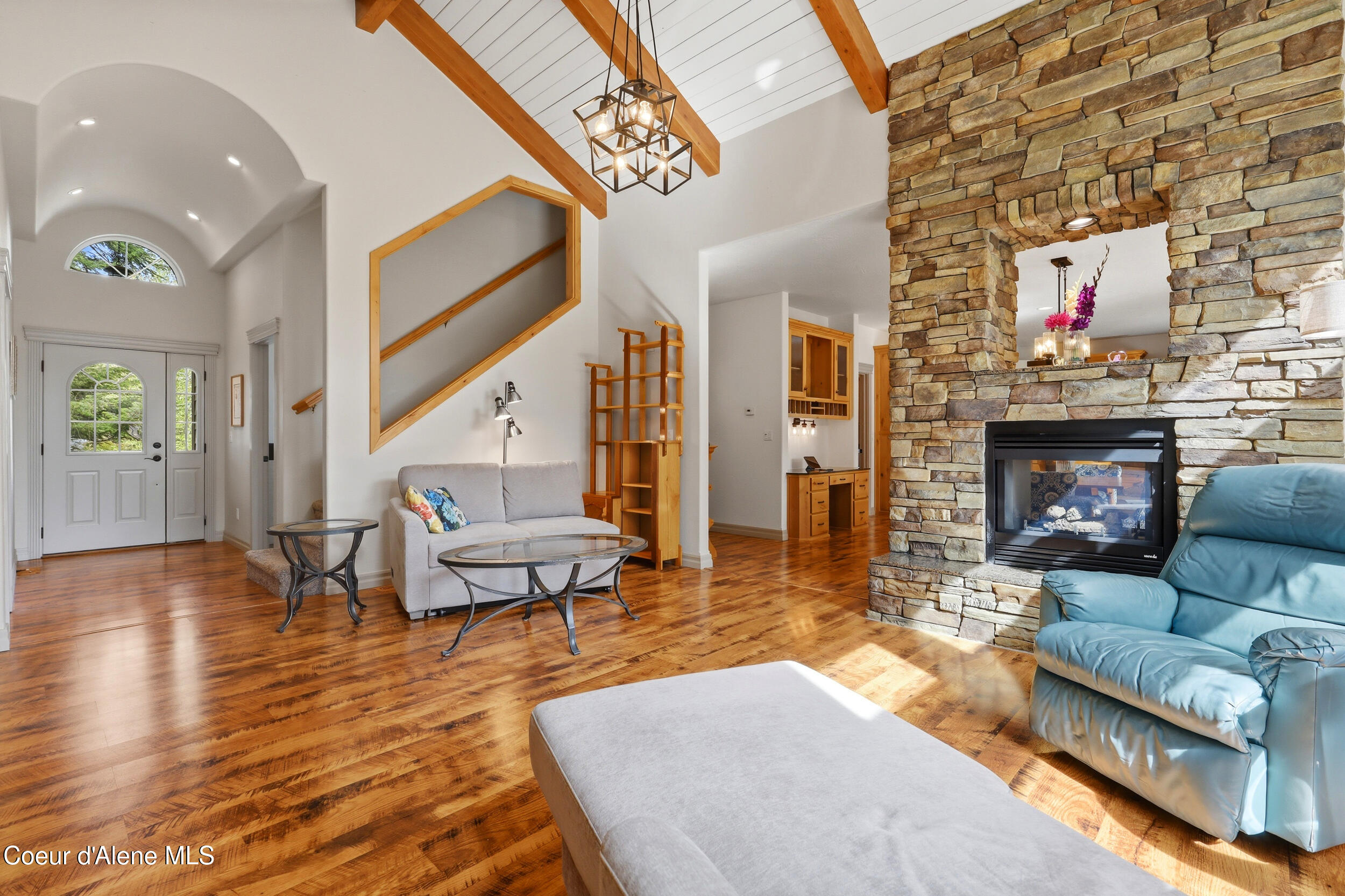 Living room with vaulted timber-beam ceiling, hardwood floors, and a large stone fireplace.
