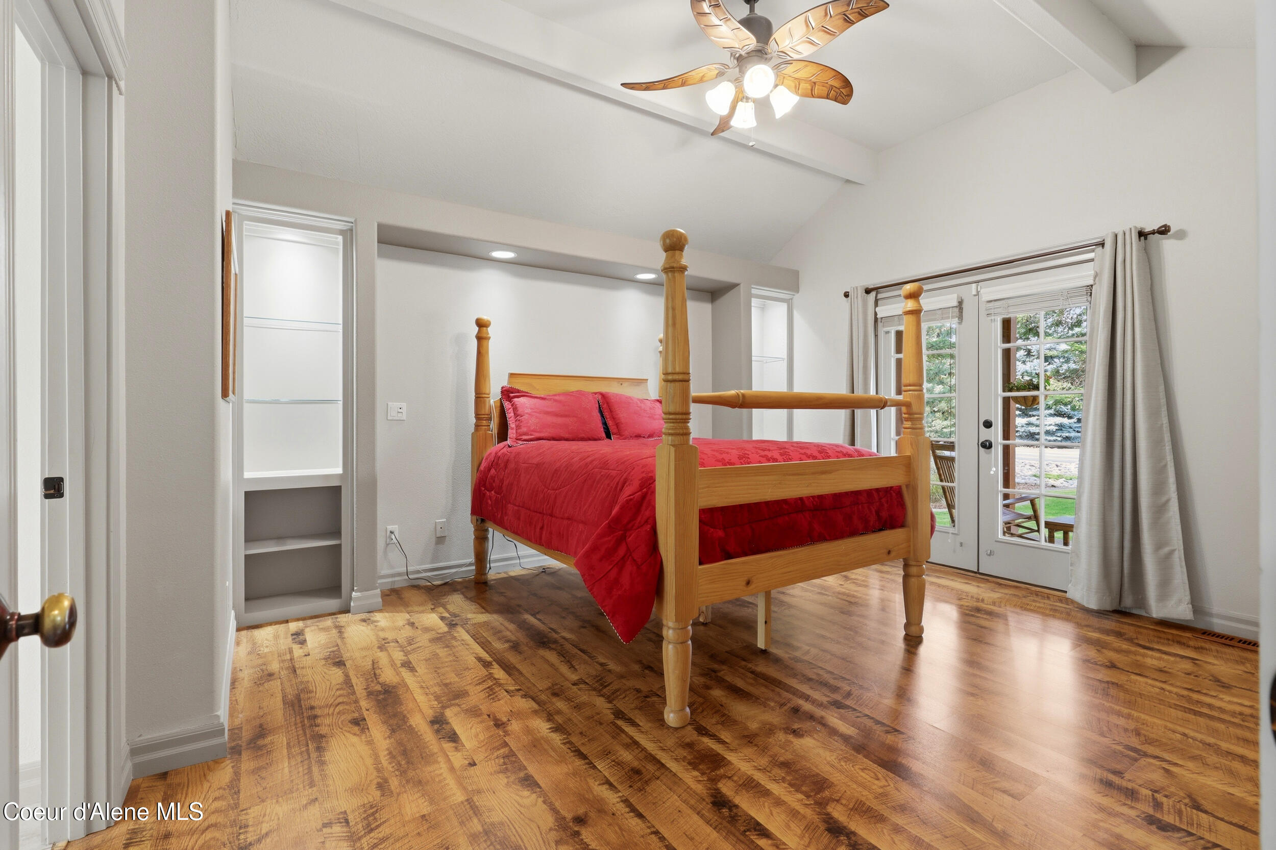 Bedroom with a wooden four-poster bed, red bedding, hardwood floors, and glass patio doors.