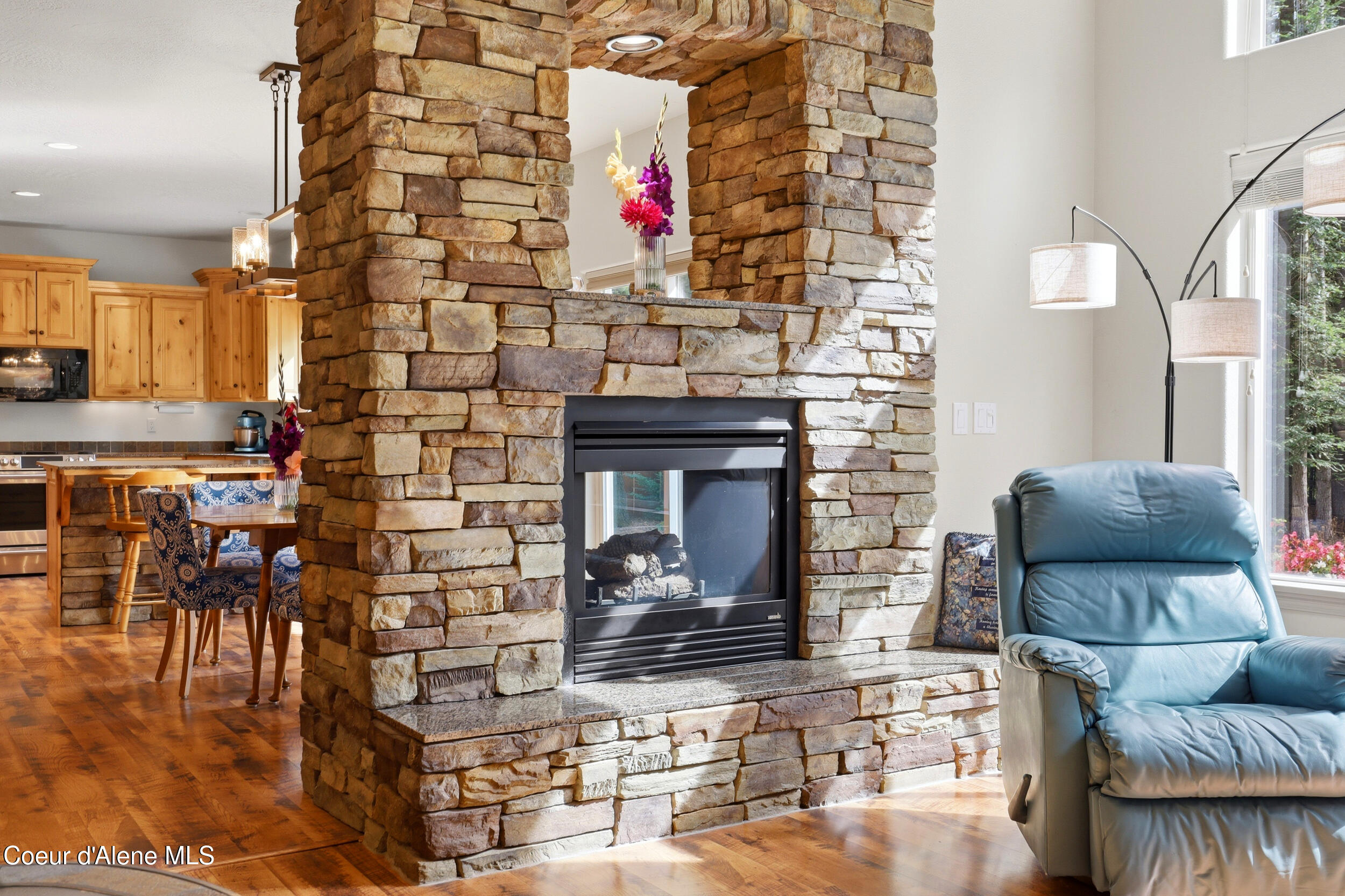 Living room with a floor-to-ceiling stone fireplace, open kitchen and dining area, and blue leather recliner.