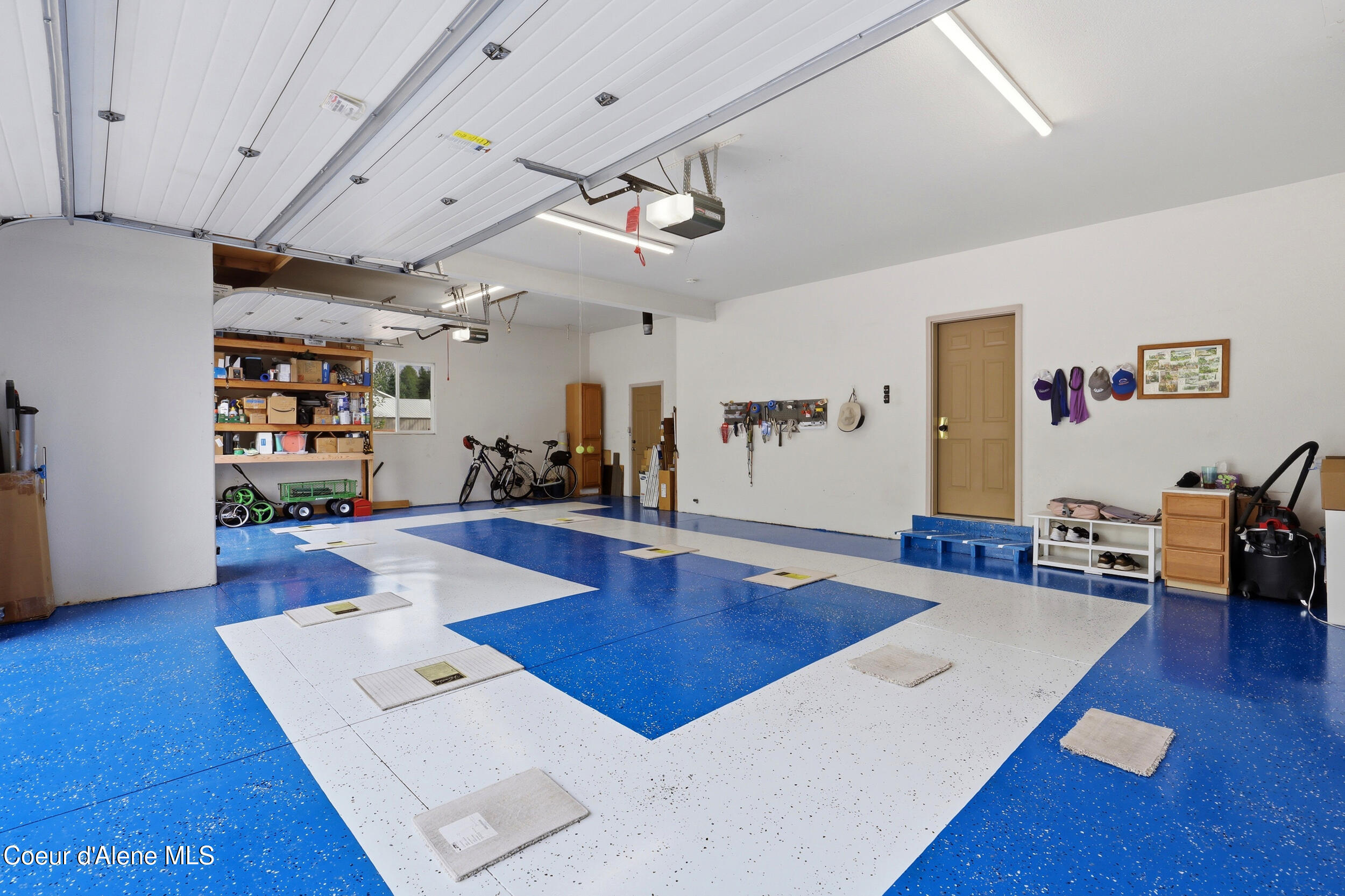 Spacious garage with a blue-and-white speckled floor, storage shelves, bicycles, and wall-mounted tools.