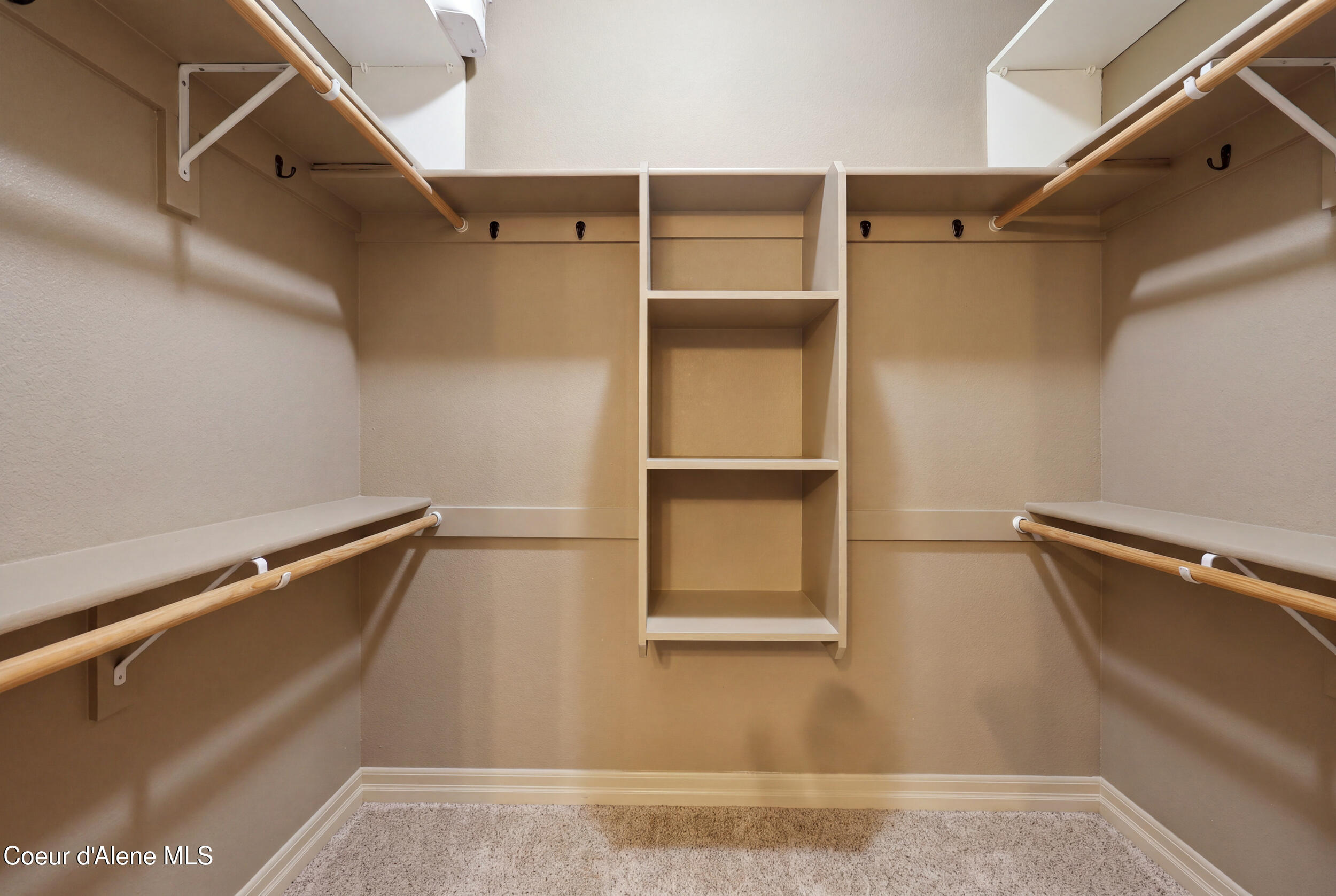 Walk-in closet with central built-in shelving, wooden hanging rods, and carpeted floor.
