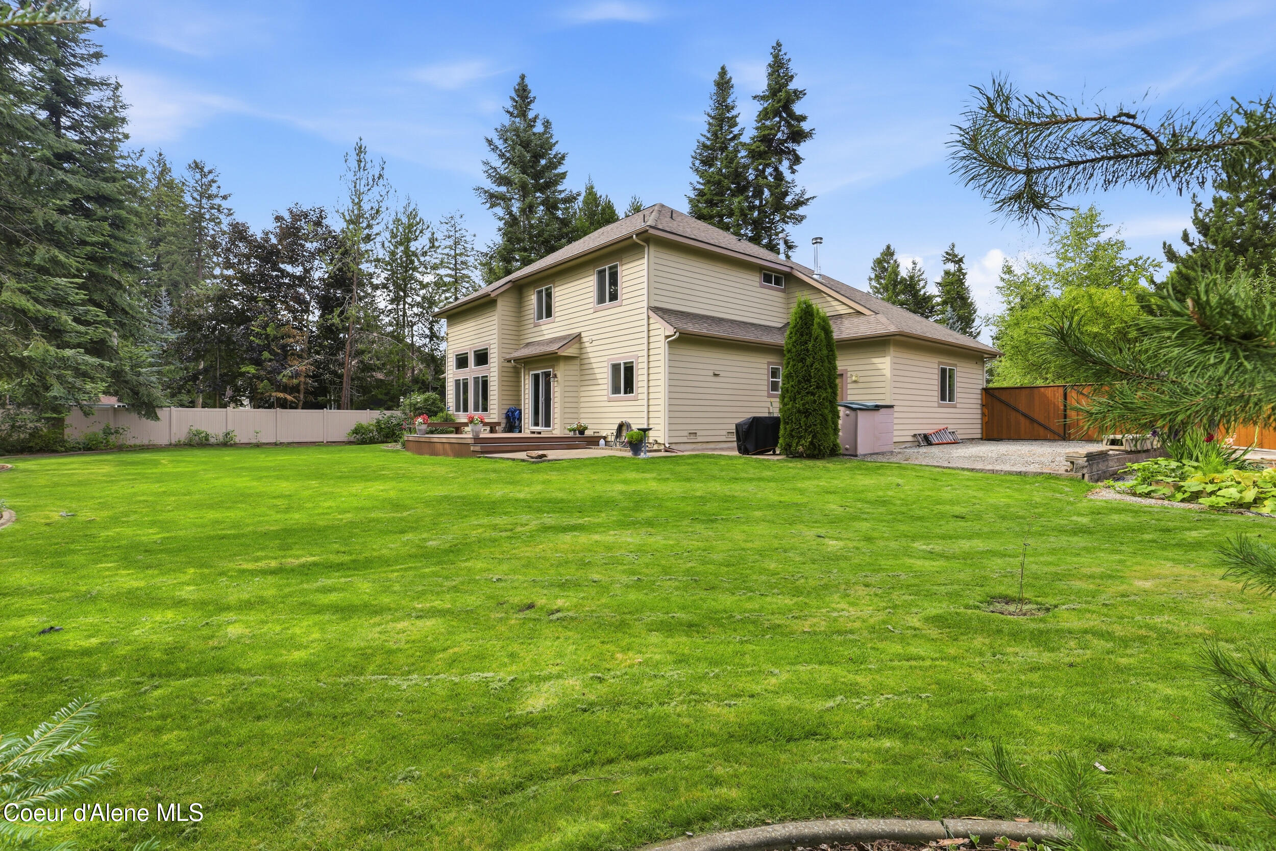 Two-story beige house behind a broad green lawn, with a small deck and fenced yard.