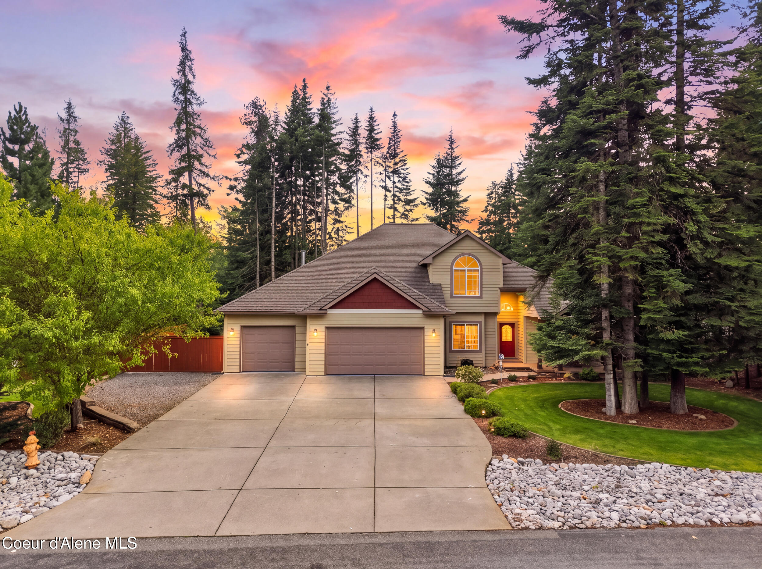 Two-story home with an attached garage, evergreen trees, and a pink-orange sunset sky.