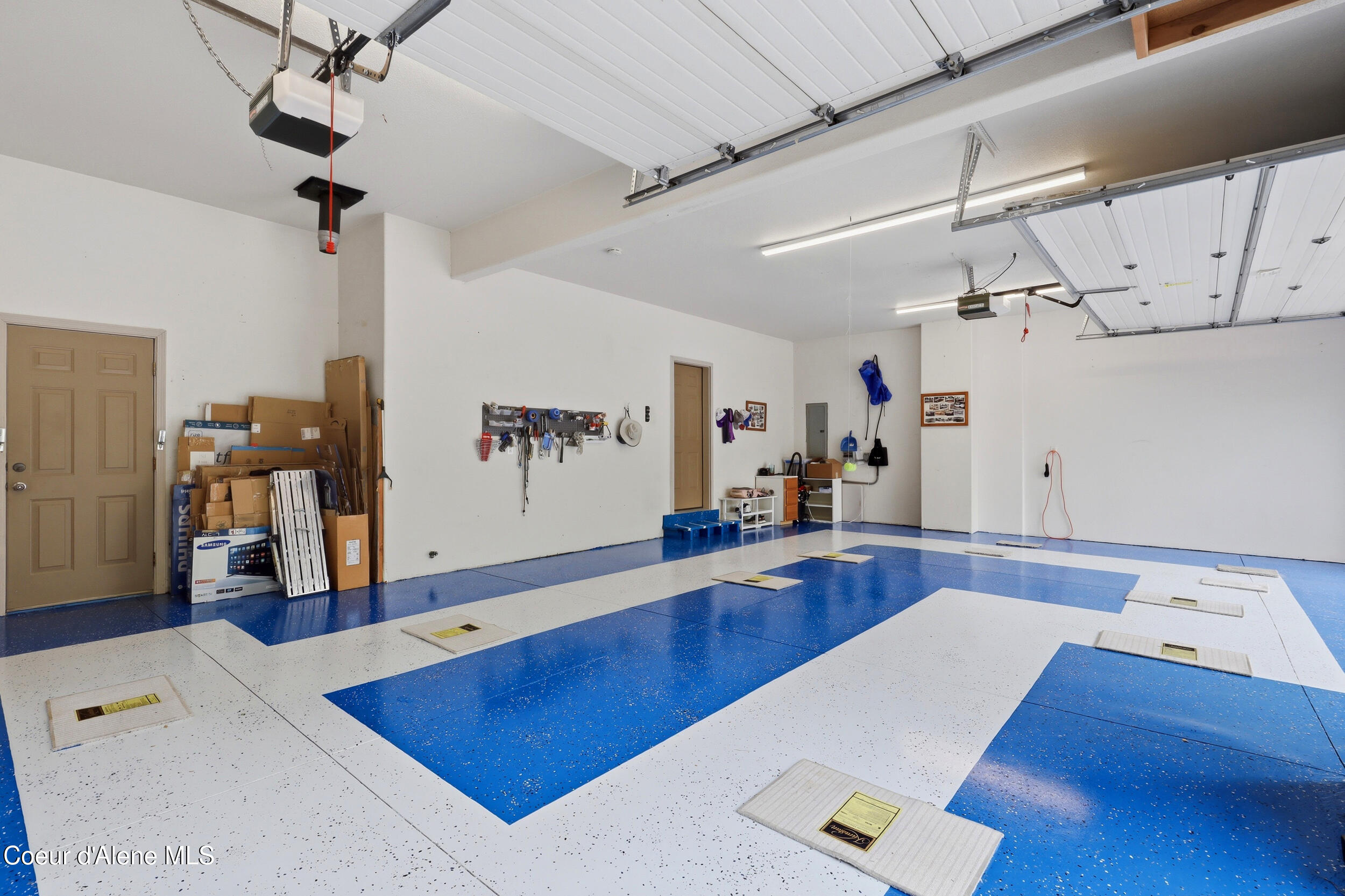 Spacious garage with a blue-and-white speckled floor, overhead doors, and wall-mounted tools.