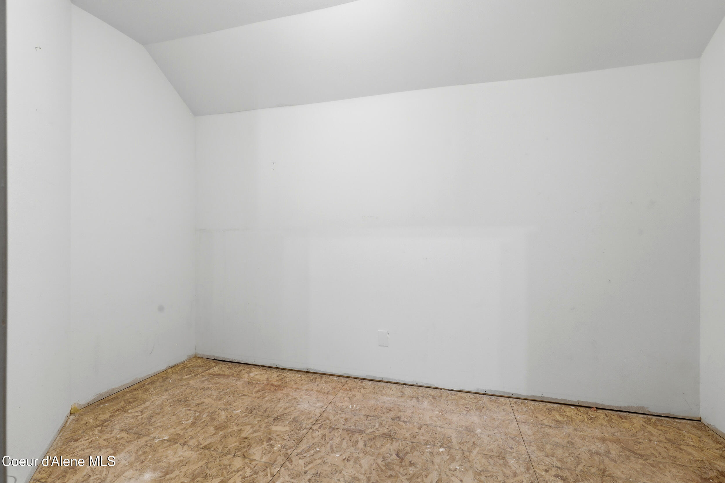 Empty unfinished room with white walls, an angled ceiling, and exposed OSB subfloor.