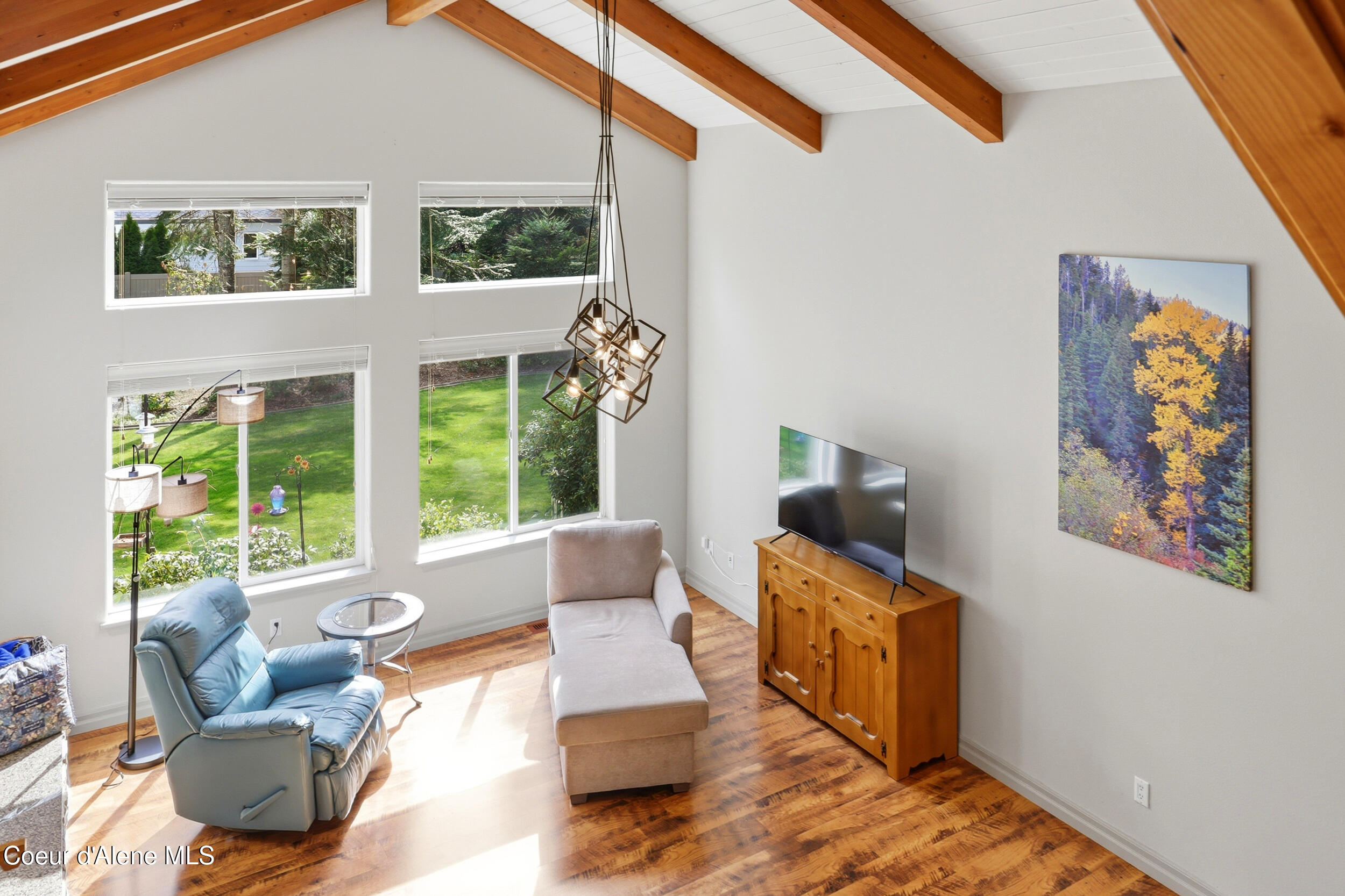 Bright living room with vaulted timber-beam ceiling, garden-facing windows, blue recliner, and chaise lounge.