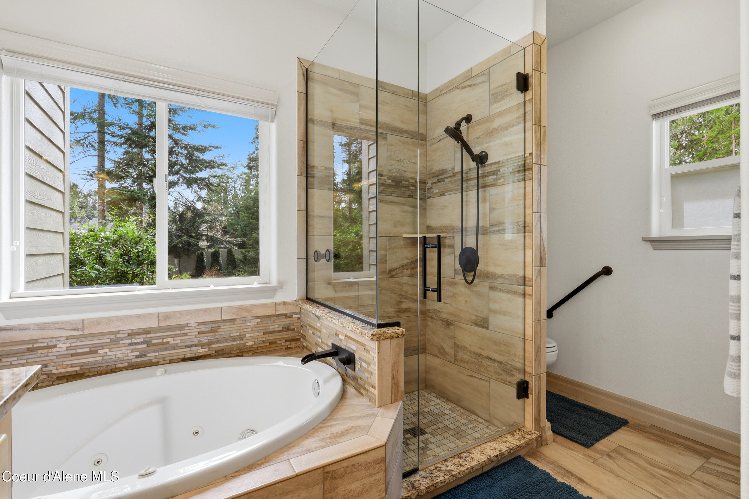 Bathroom with a jetted soaking tub, tiled glass shower, and large window overlooking trees.