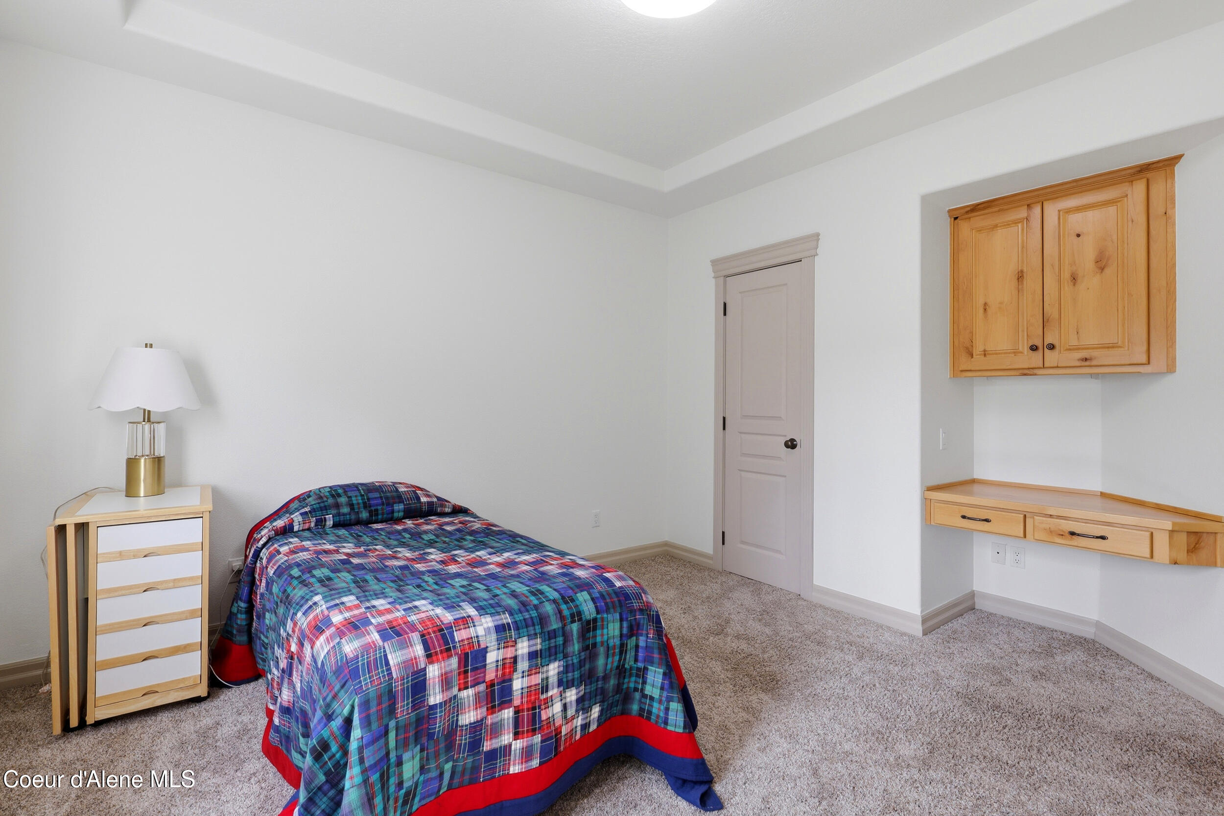 Bedroom with a plaid-covered bed and built-in wooden desk and cabinets.