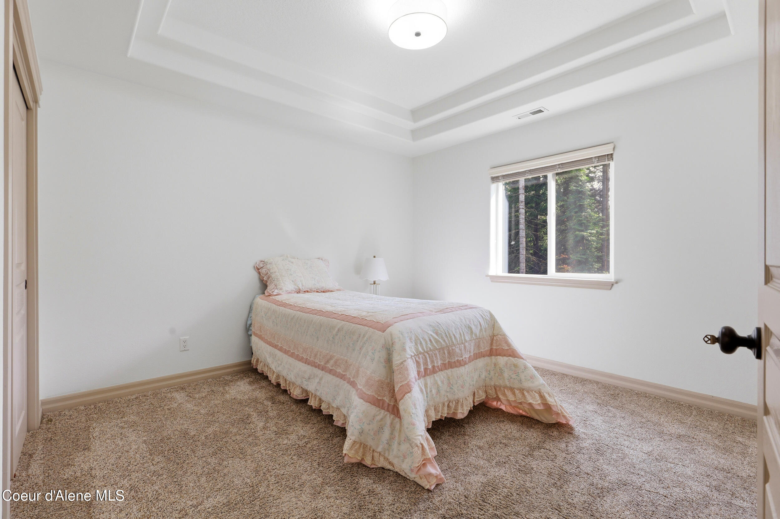 Bedroom with a single bed in a pale floral quilt and a window overlooking trees.