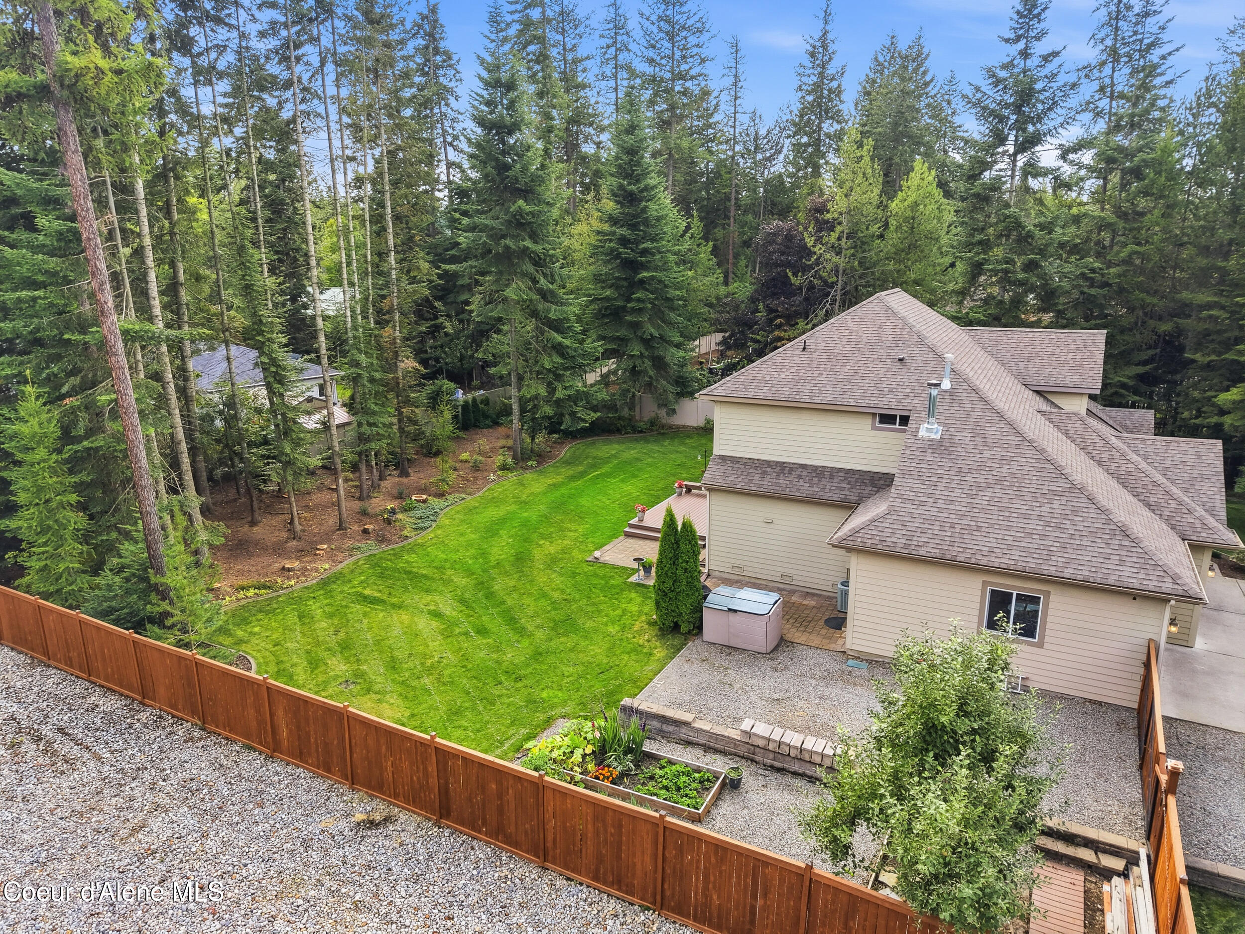 Aerial view of a beige home and fenced lawn bordered by dense evergreen trees.
