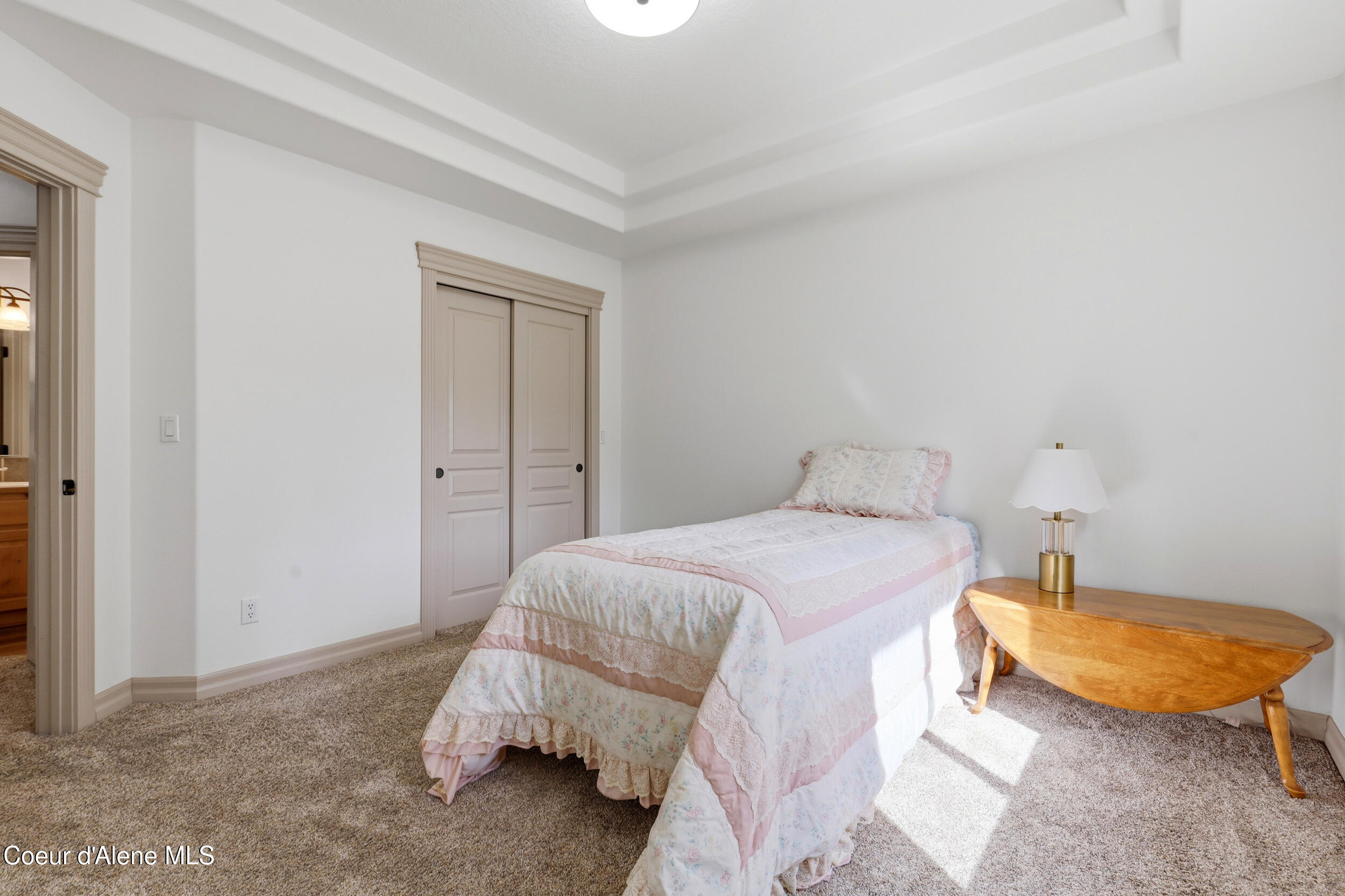 Bedroom with a single bed in pale pink floral bedding beside a wooden table and lamp.