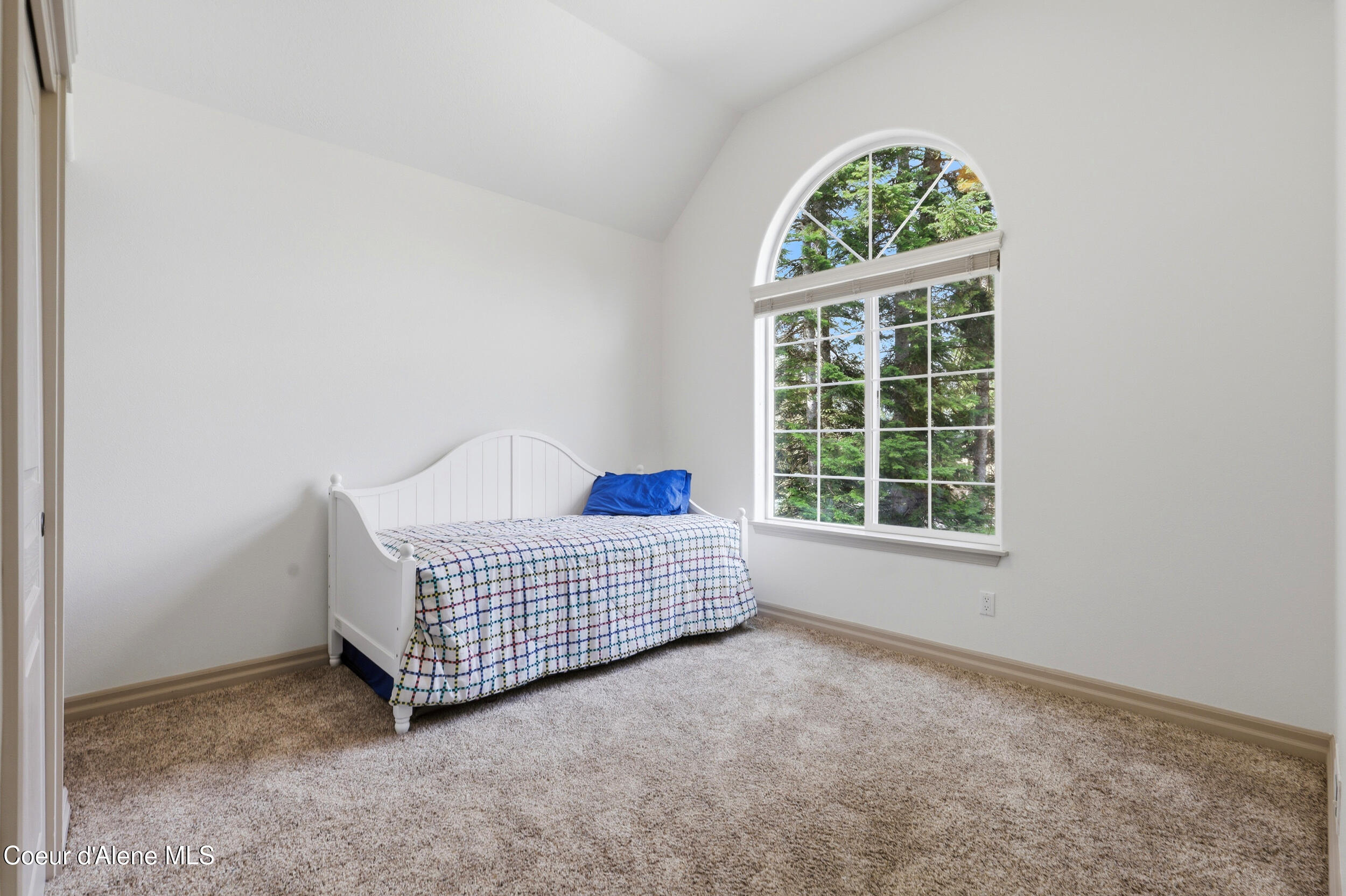 Bedroom with a white single bed beneath a large arched window overlooking trees.