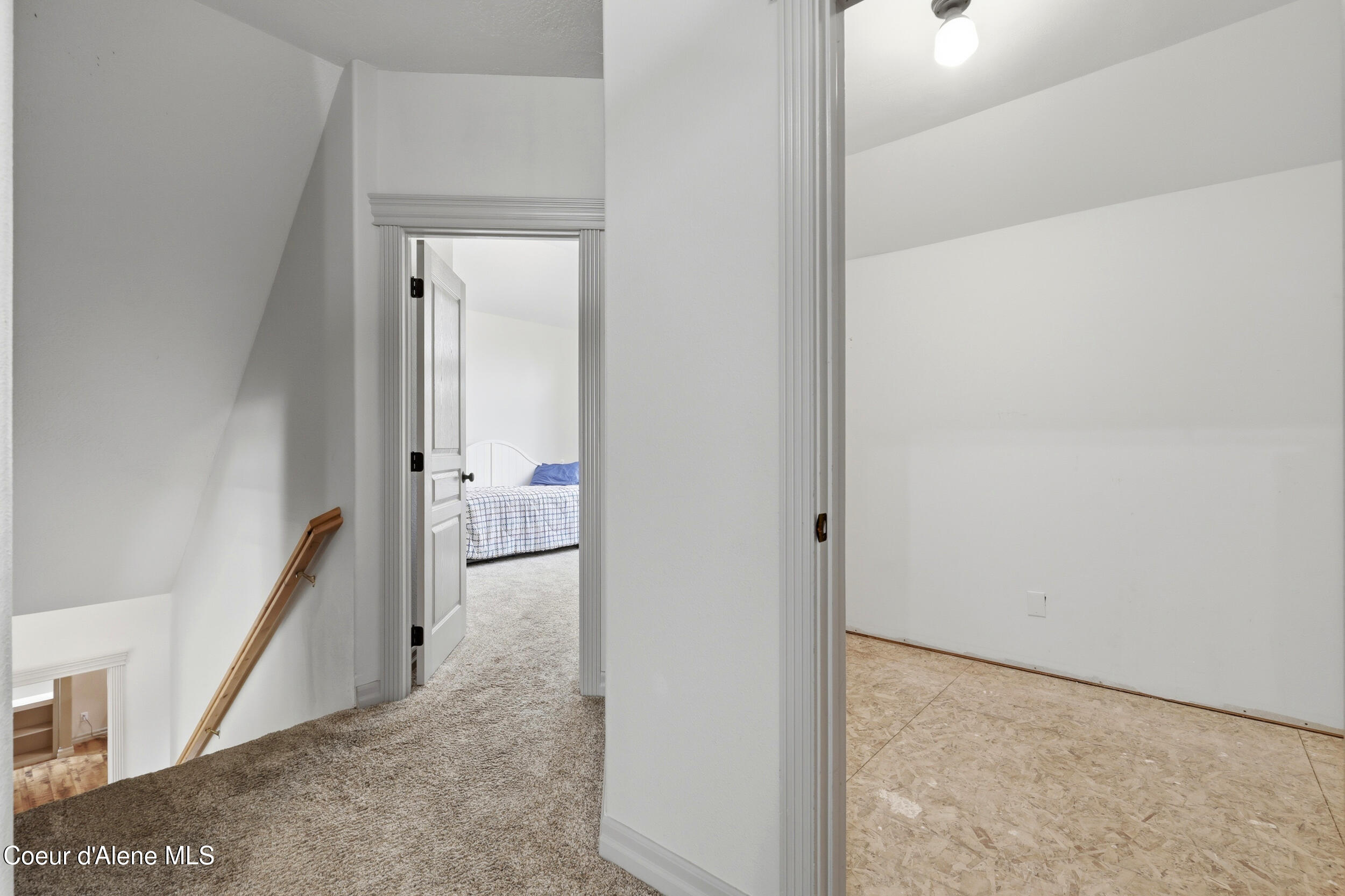 Upstairs landing beside an empty room, with a bedroom and bed visible through an open doorway.