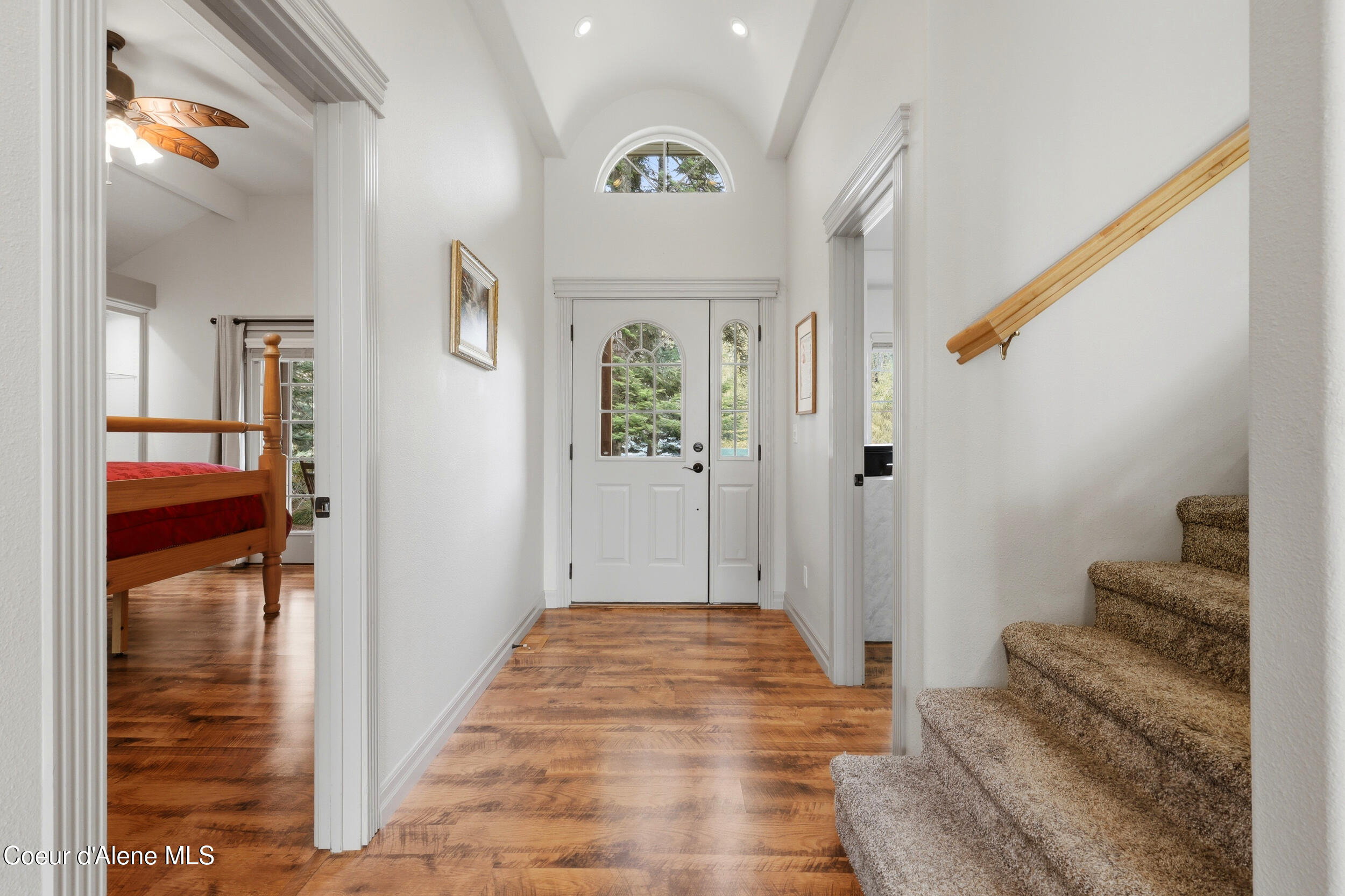 Entry foyer with arched window, wood floors, carpeted stairs, and a bedroom visible through the doorway.