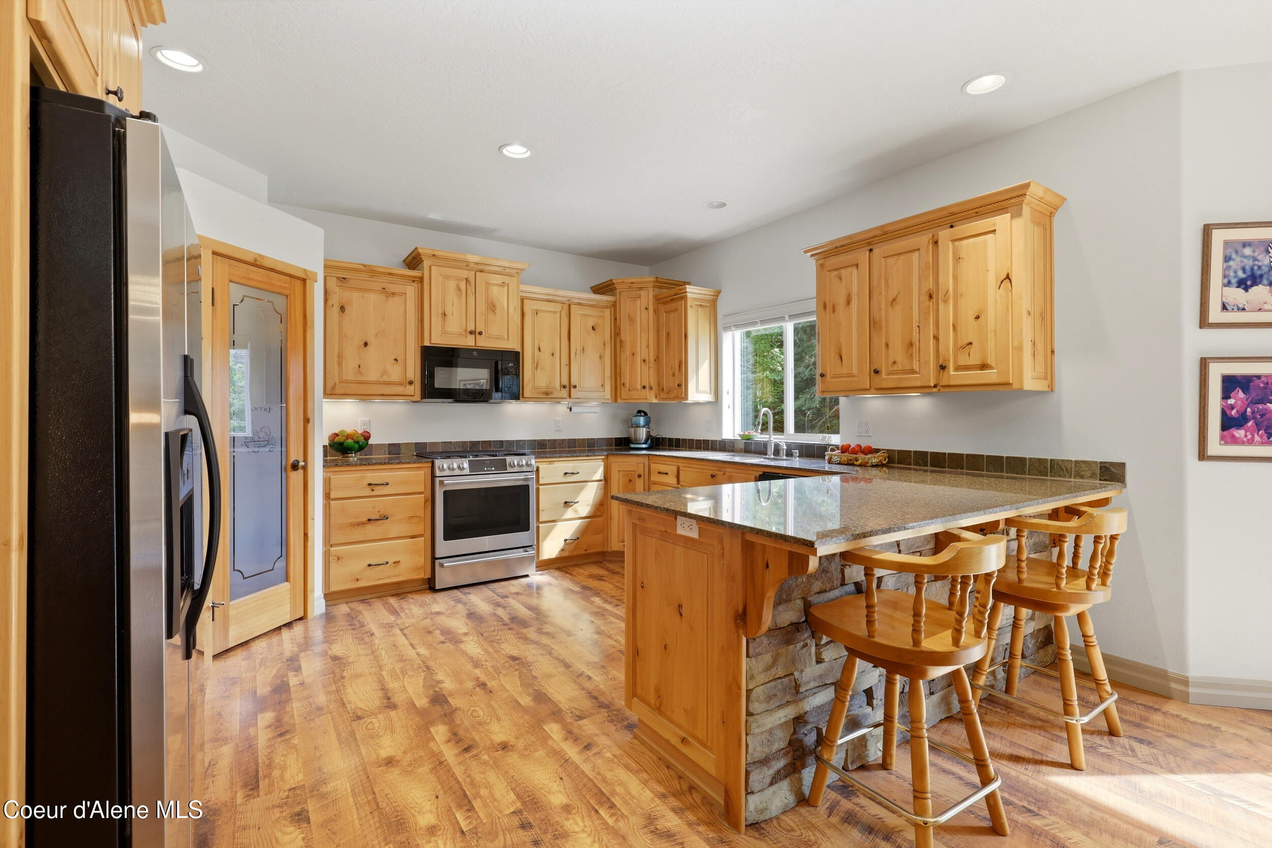 Kitchen with honey-toned cabinets, stainless appliances, and a large stone-faced island with bar stools.