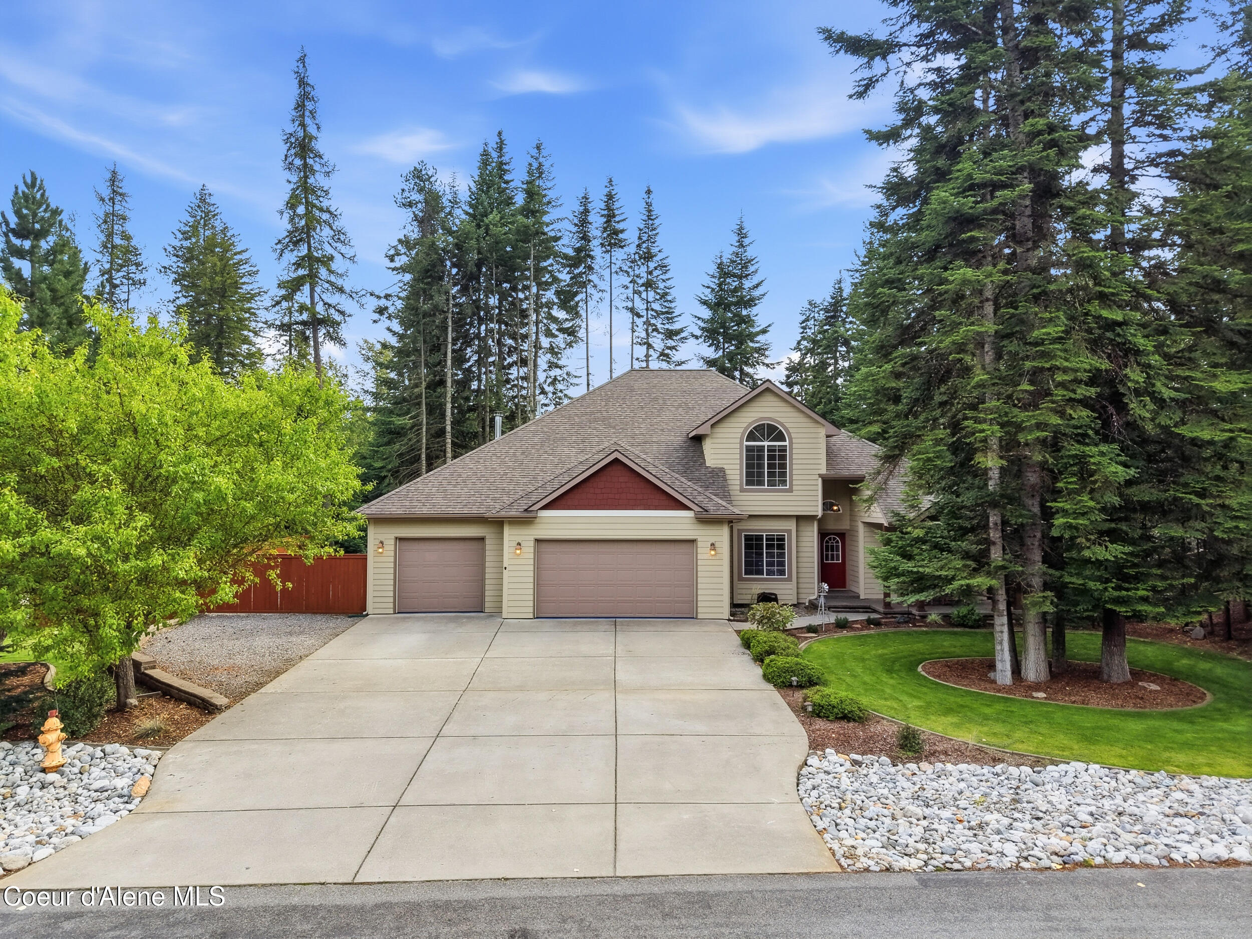 Two-story beige home with an attached garage, broad driveway, and tall evergreens.