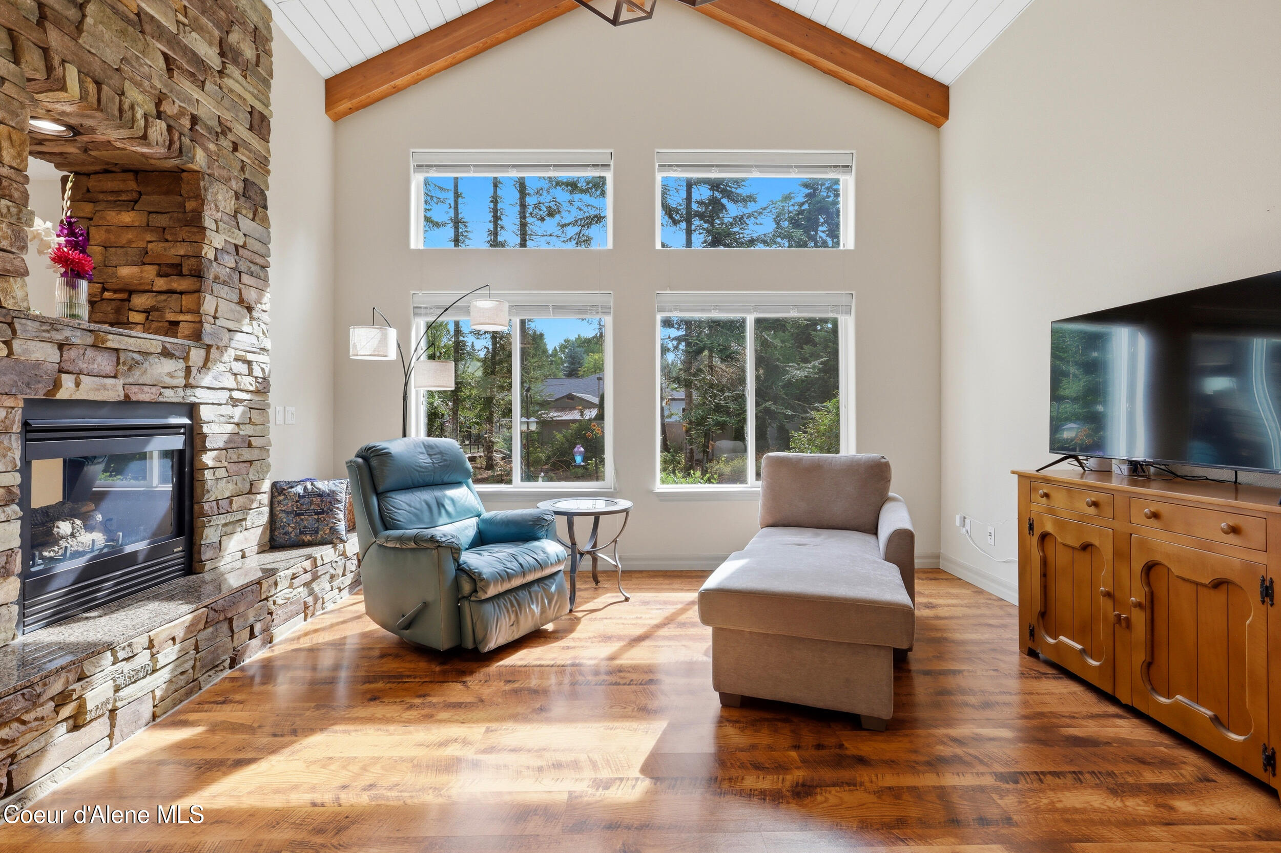 Living room with a stone fireplace, vaulted wood-beam ceiling, and large windows.