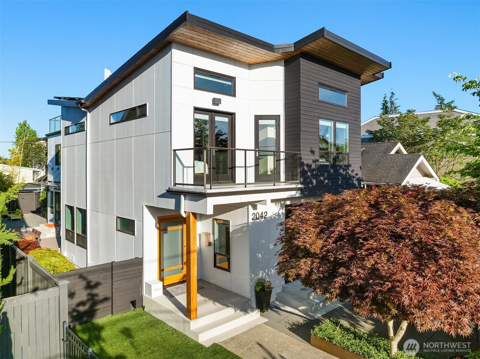 Modern two-story home with white and charcoal siding, wood accents, and a glass-railed balcony.
