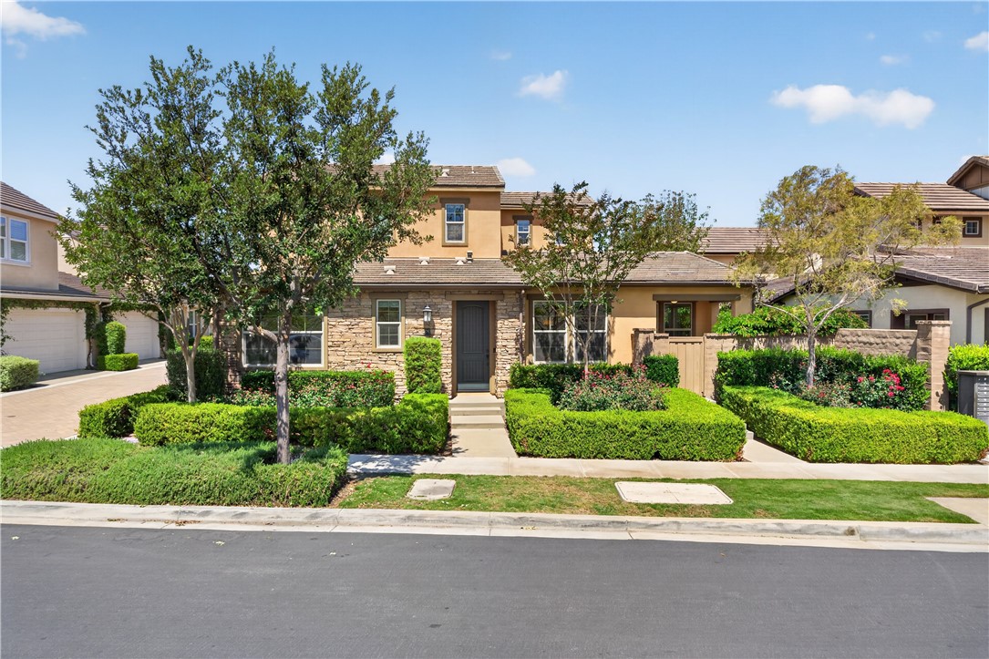 Two-story home with a stone facade, dark front door, and neatly trimmed garden beds.
