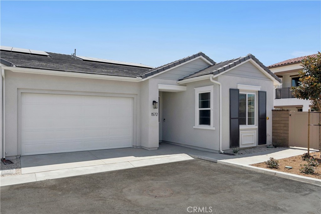 Single-story gray stucco home with solar panels, a wide garage door, and recessed front entrance.