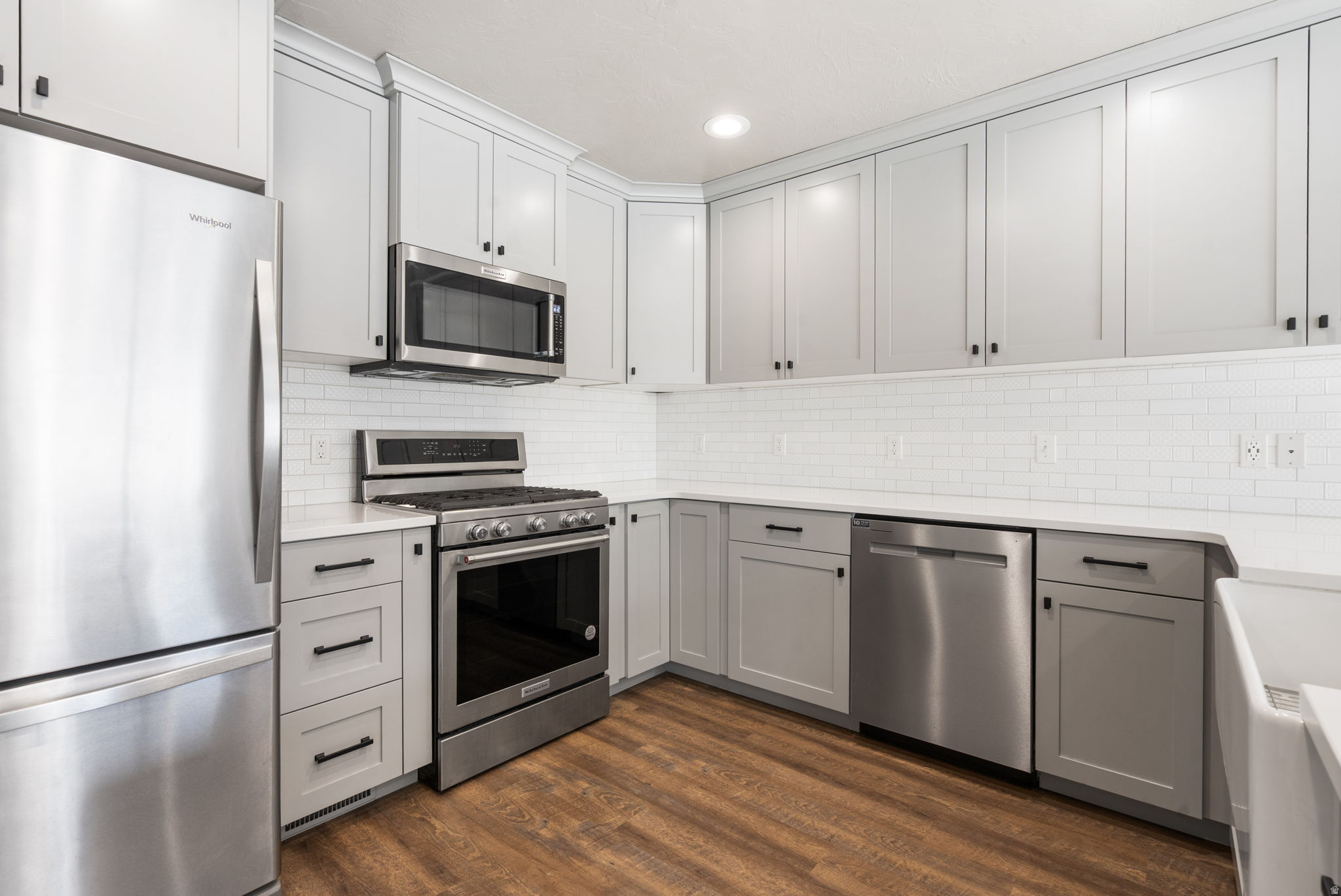 Kitchen with white shaker cabinets, stainless steel appliances, subway tile backsplash, and wood flooring.