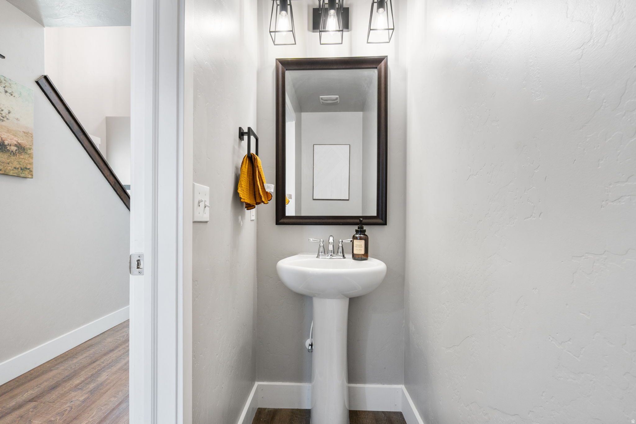 Powder room with a pedestal sink, dark-framed mirror, and mustard-yellow hand towels.