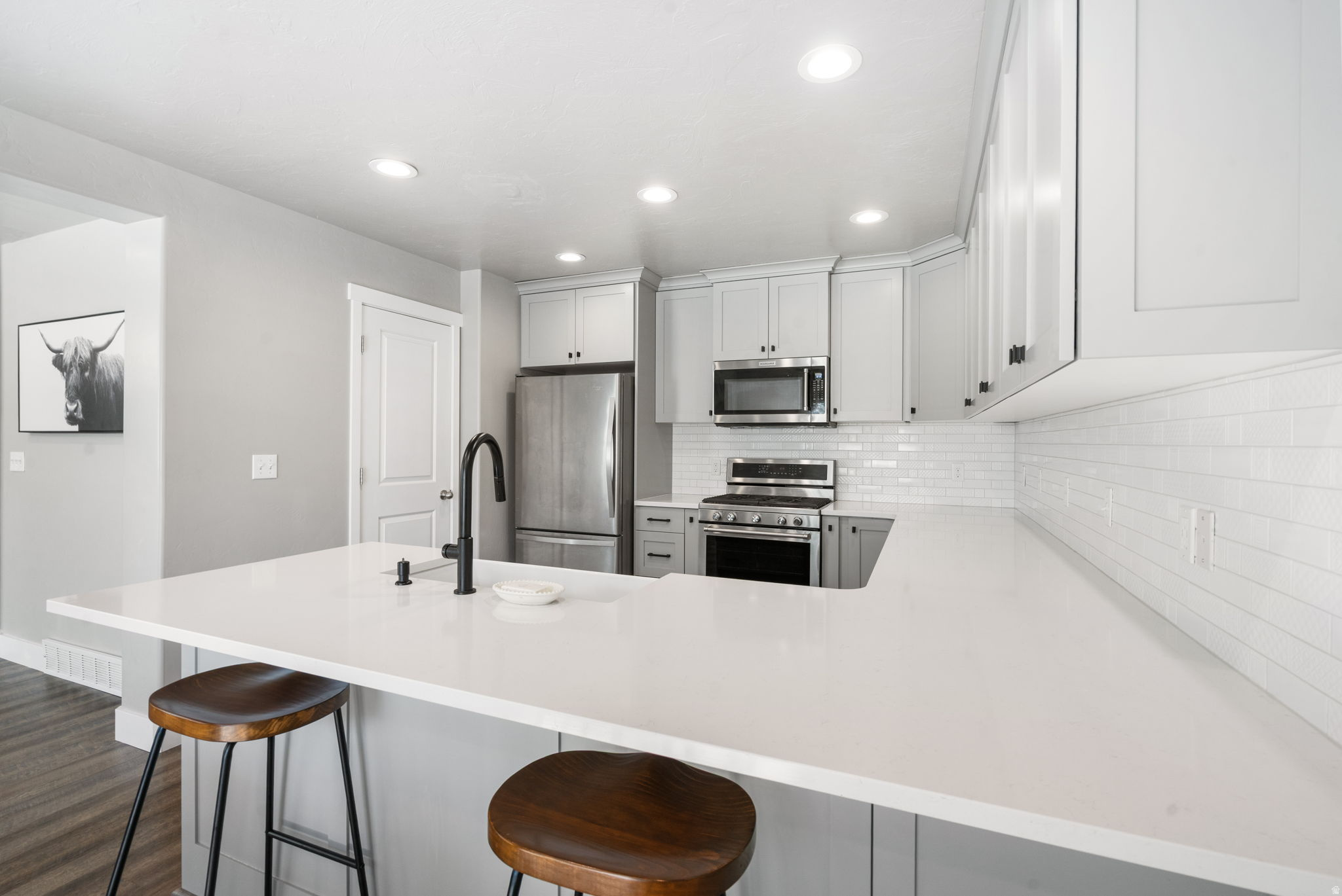 Modern kitchen with white cabinets, stainless steel appliances, and a large island with wooden stools.