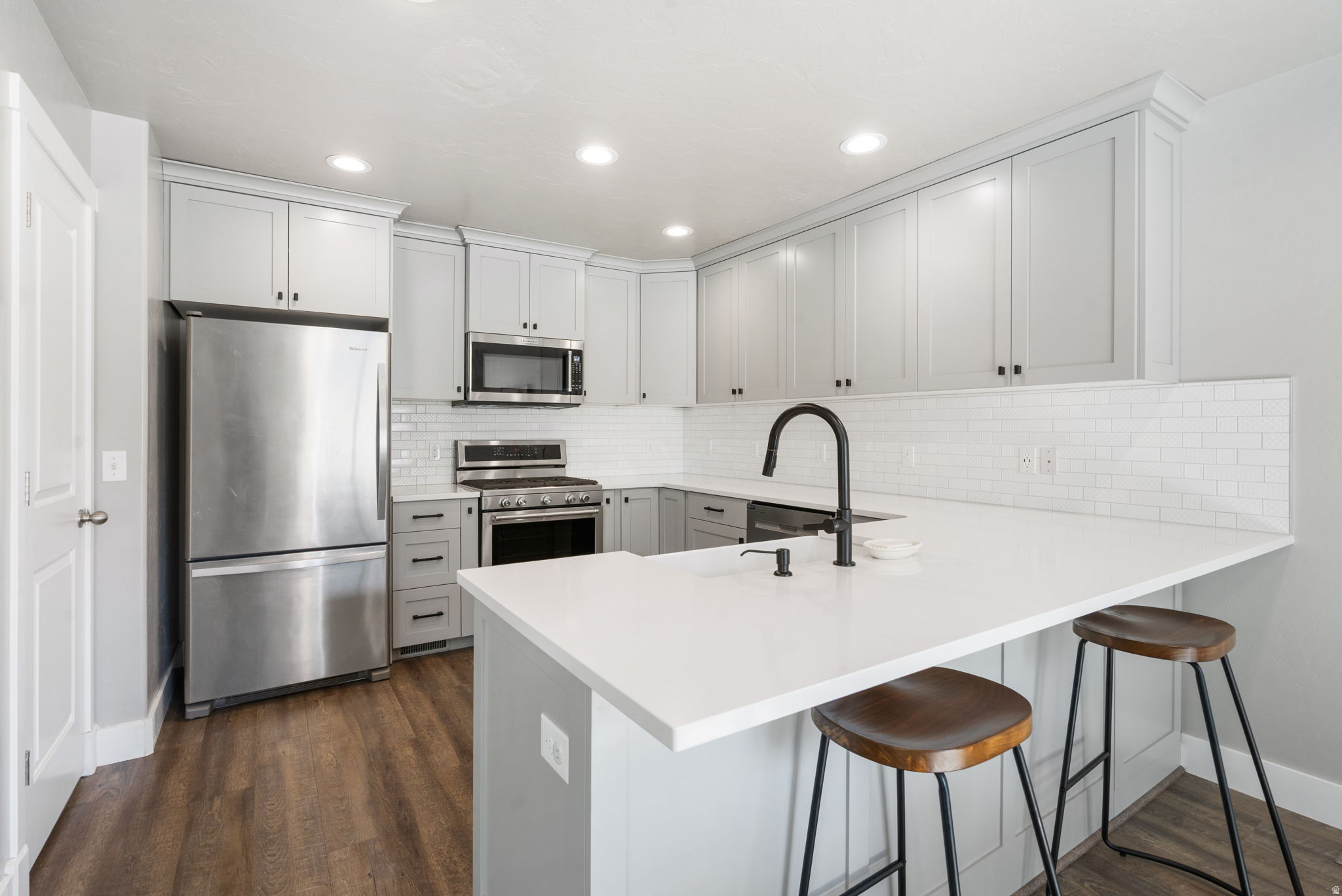 Kitchen with gray cabinets, stainless steel appliances, and a large white island with two stools.