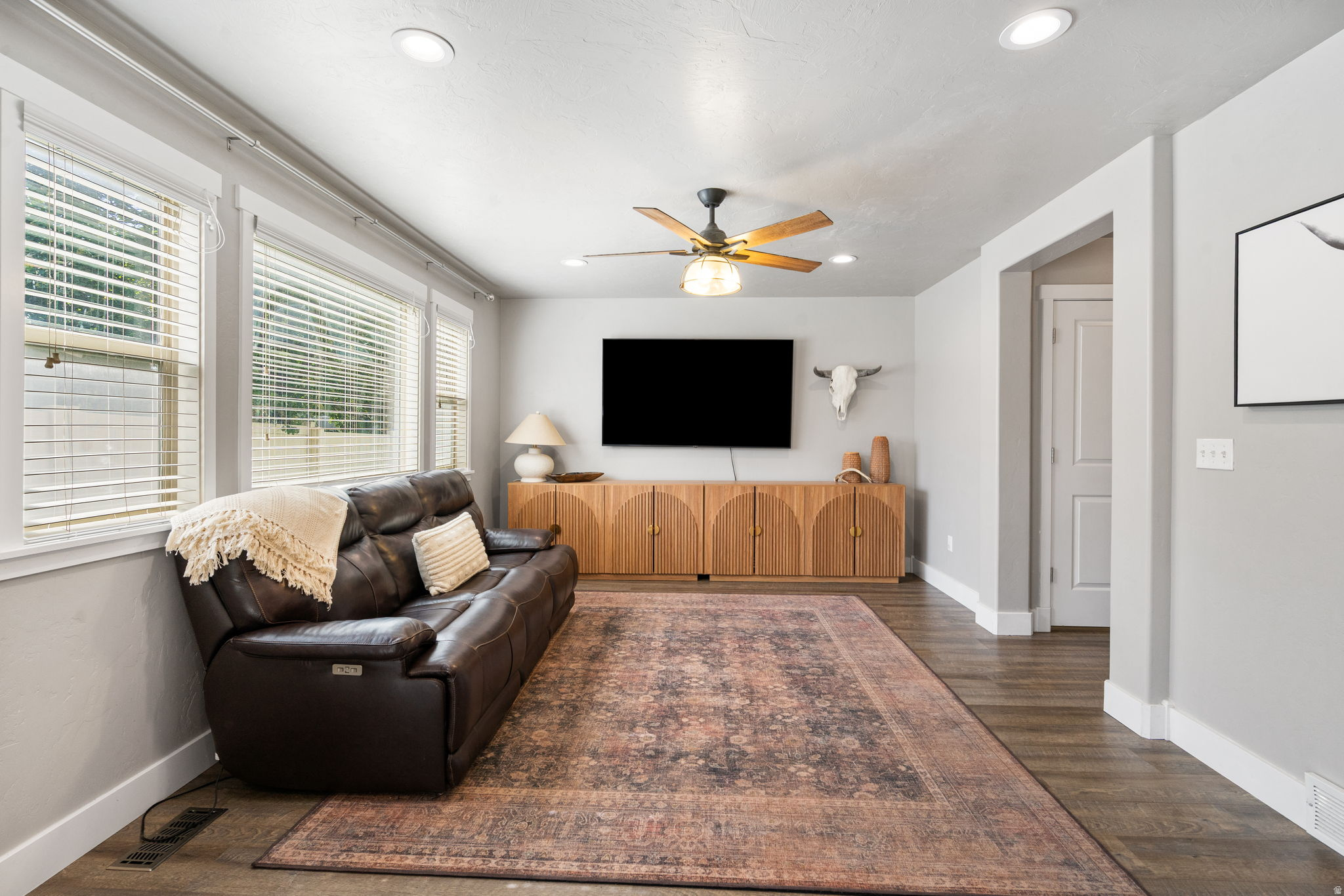 Living room with a leather sofa, patterned rug, wood media cabinet, and wall-mounted television.