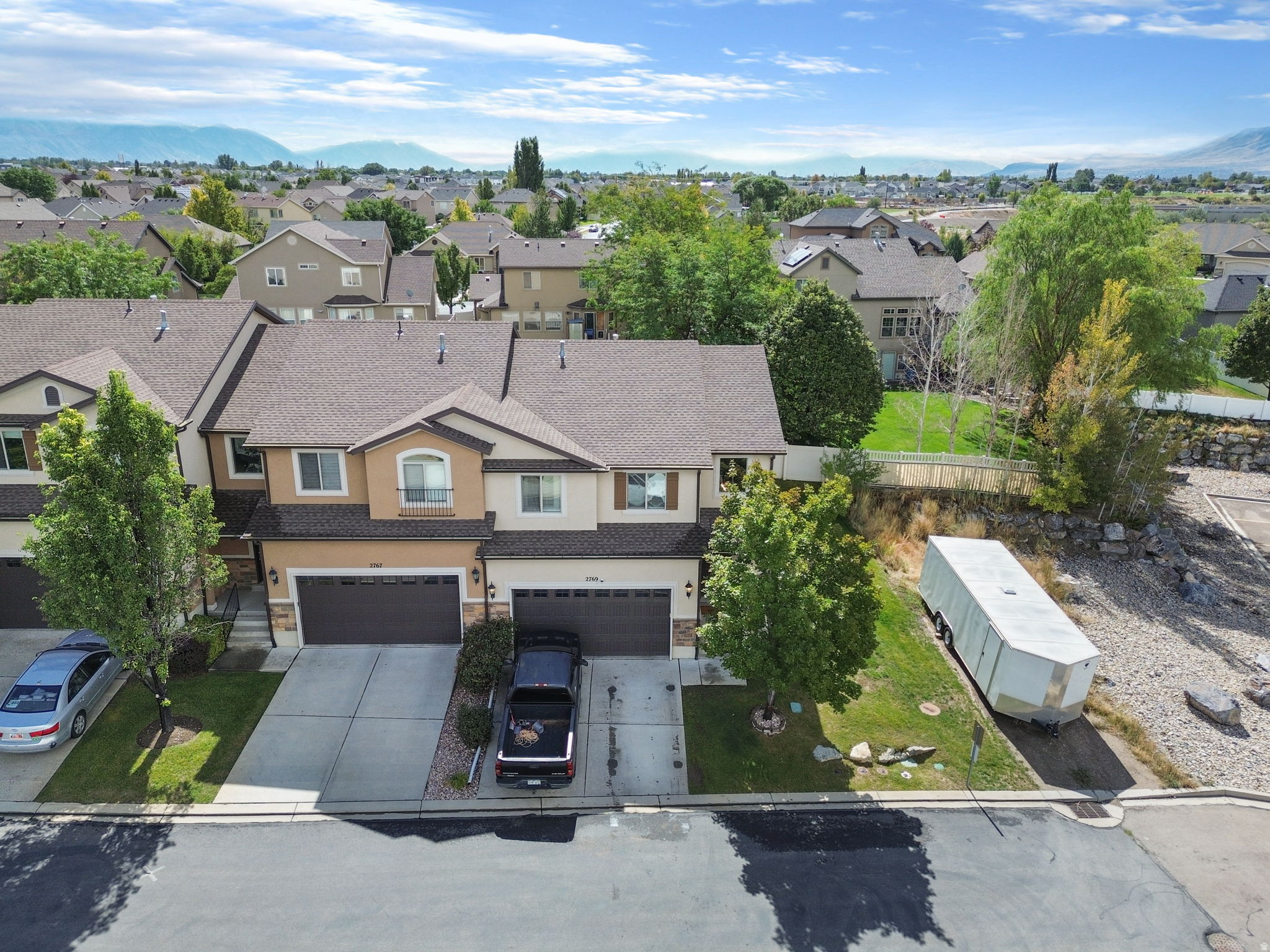 Aerial view of a two-story home with an attached garage, landscaped yard, and mountains in the distance.