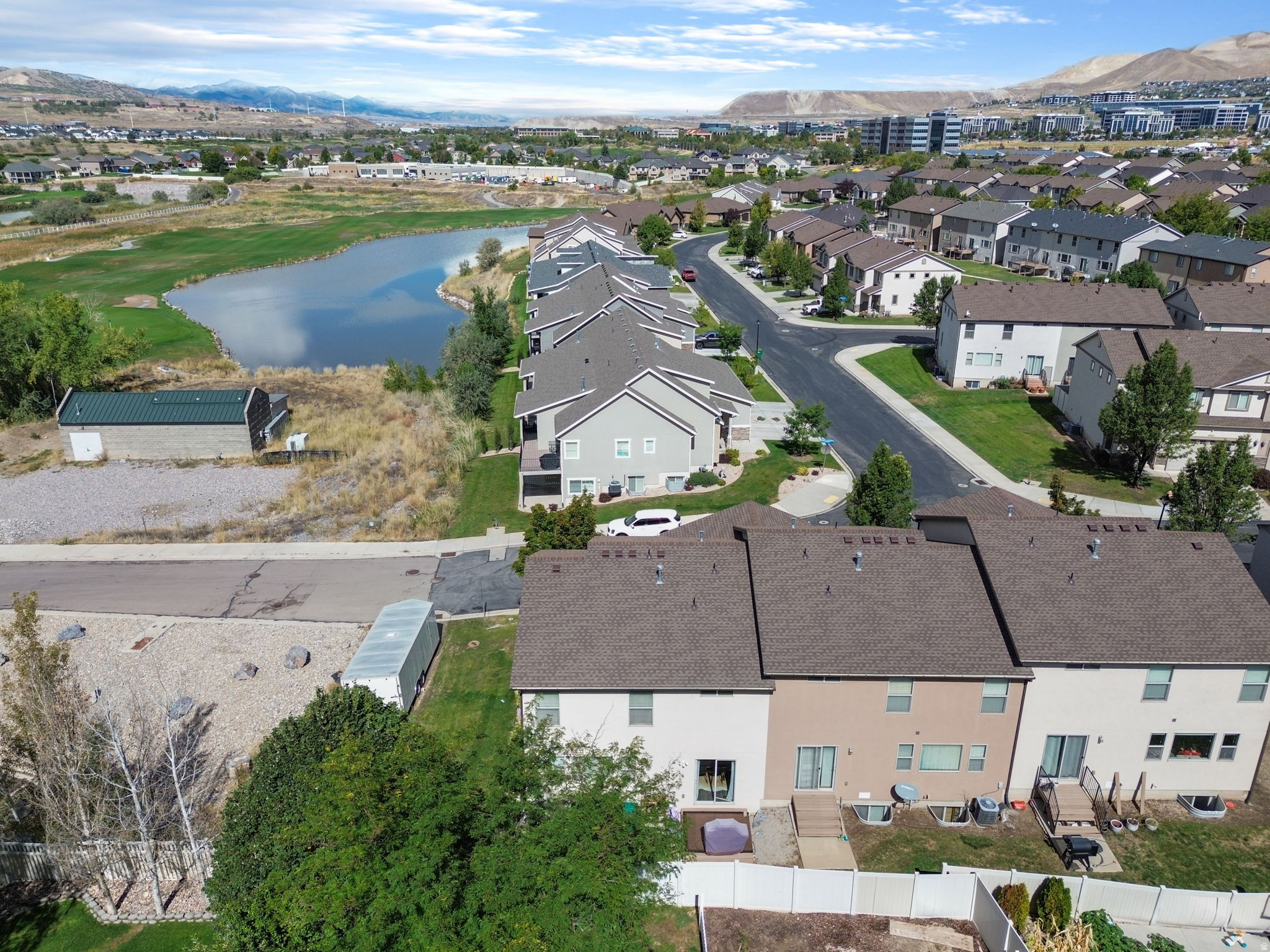 Aerial view of attached homes beside a pond, with neighborhood streets and mountains beyond.