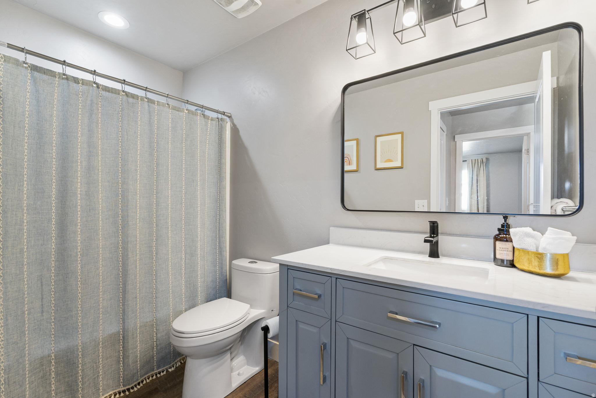 Bathroom with a blue-gray vanity, black faucet, large mirror, and patterned gray shower curtain.