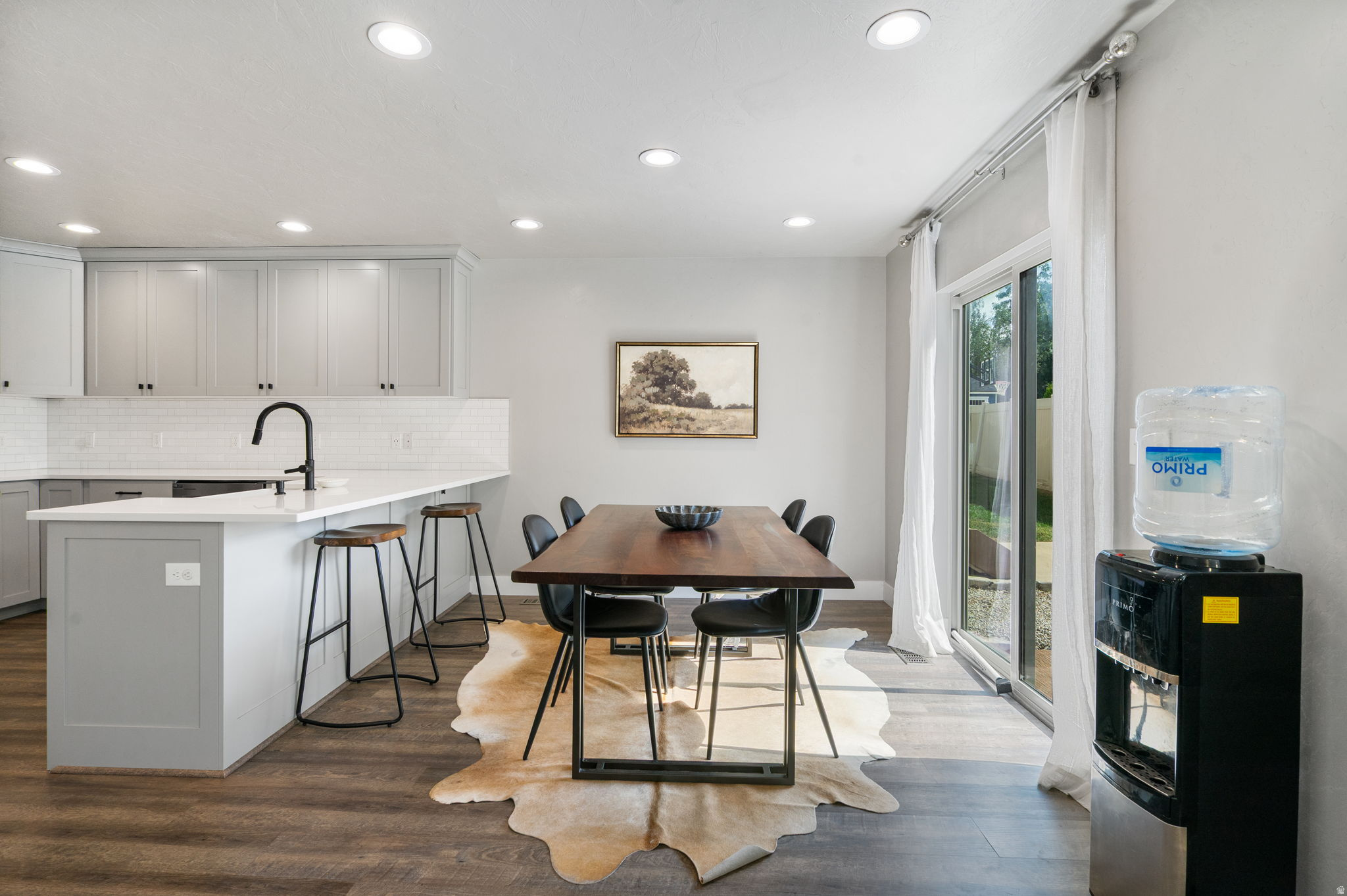 Dining area with a dark wood table on a hide rug beside a gray-and-white kitchen.