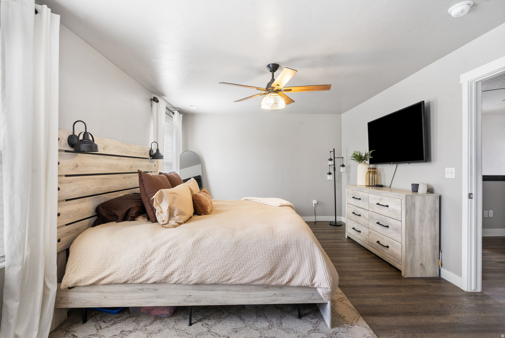 Bedroom with a pale wood platform bed, plank headboard, and wall-mounted television above a dresser.