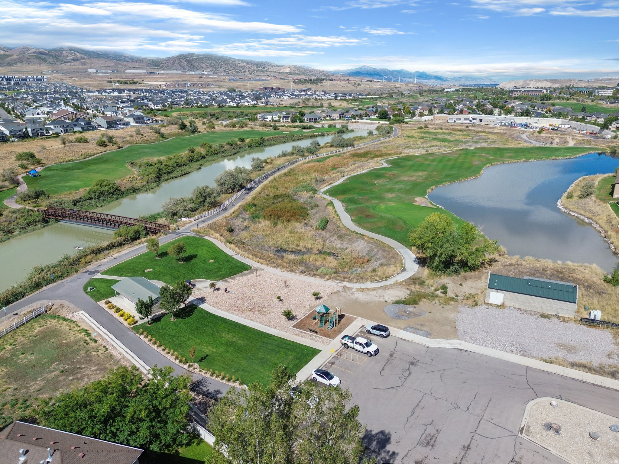 Aerial view of a neighborhood park with ponds, a bridge, winding paths, and distant mountains.
