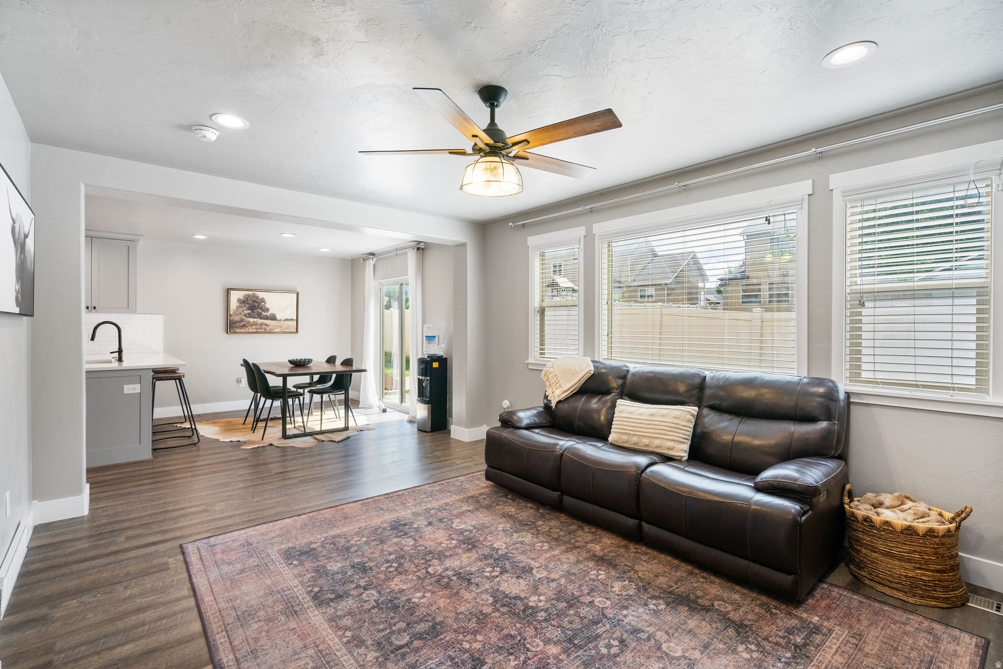 Open-plan living room with leather sofa, large windows, and dining area beside the kitchen.